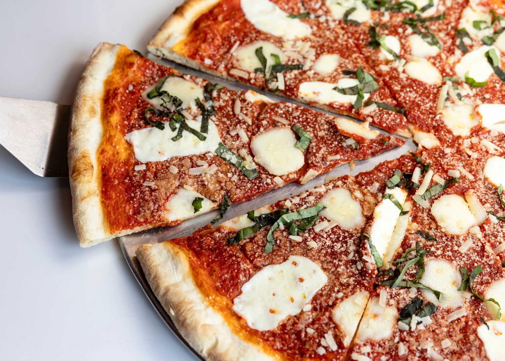 Close-up of a cheese and tomato pizza with basil on a silver tray.