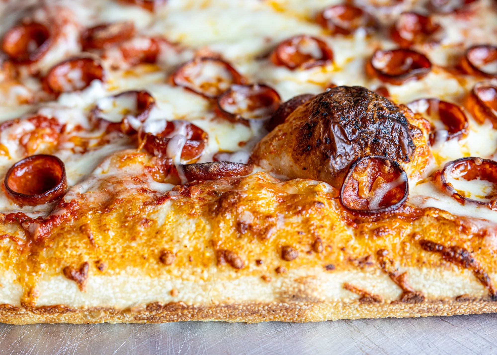 Close-up of a meatlover's pizza with pepperoni, sausage, cheese, and a thick crust.
