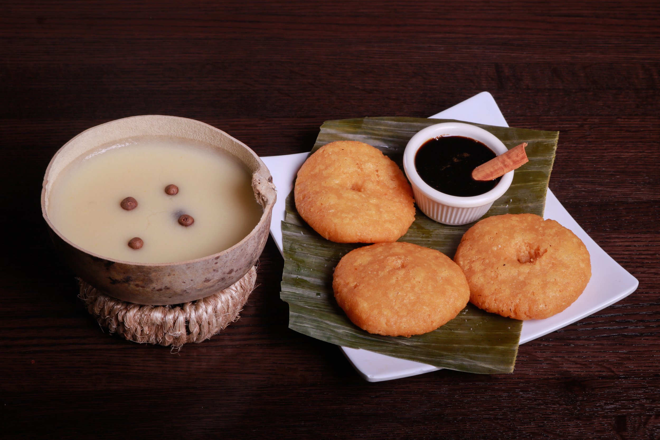 Traditional Latin American meal with fried corn cakes, dark dipping sauce, and a creamy beverage served in a coconut bowl