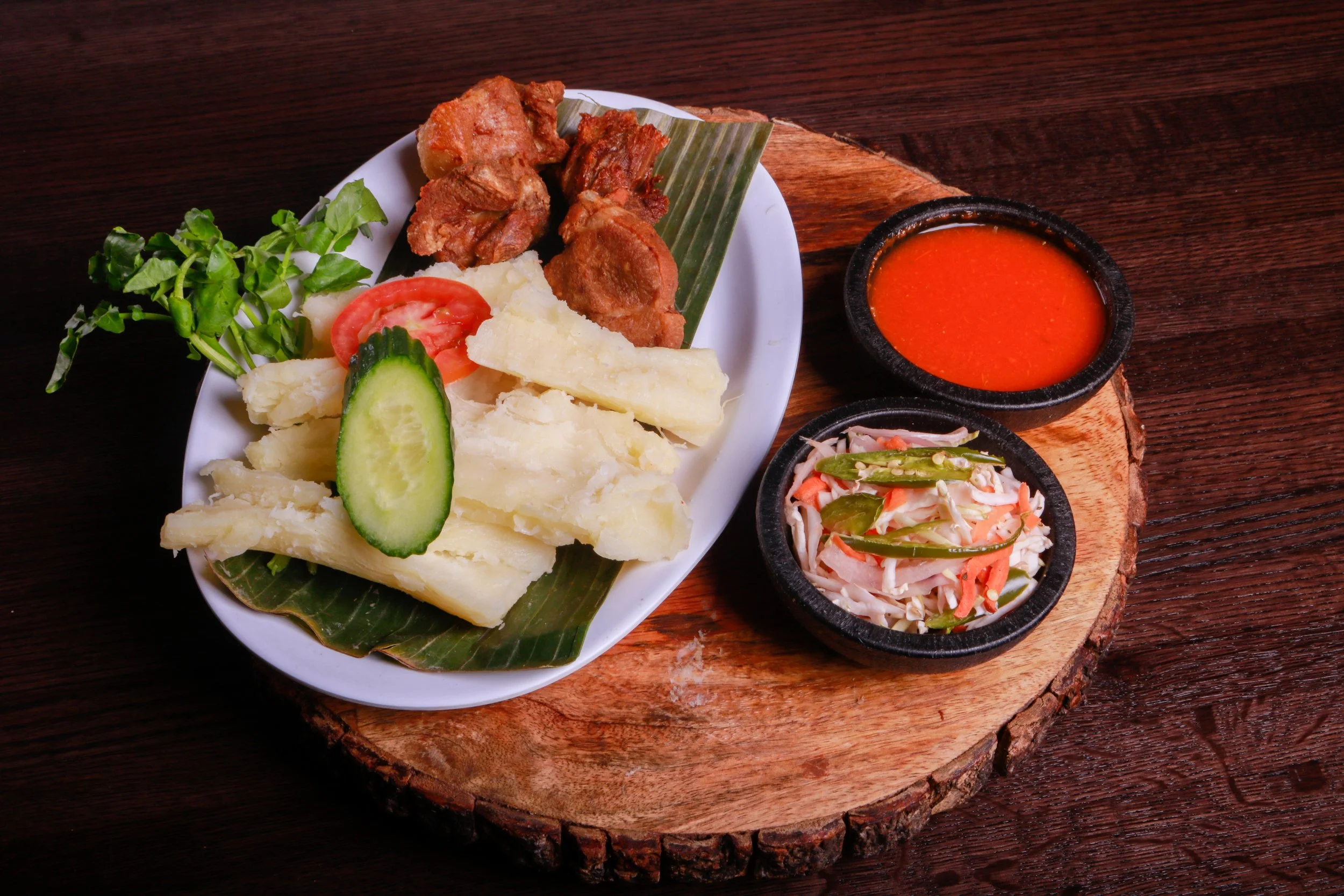 Traditional Latin American plate with fried pork, boiled yuca, tomato, cucumber, greens, spicy red sauce, and cabbage slaw