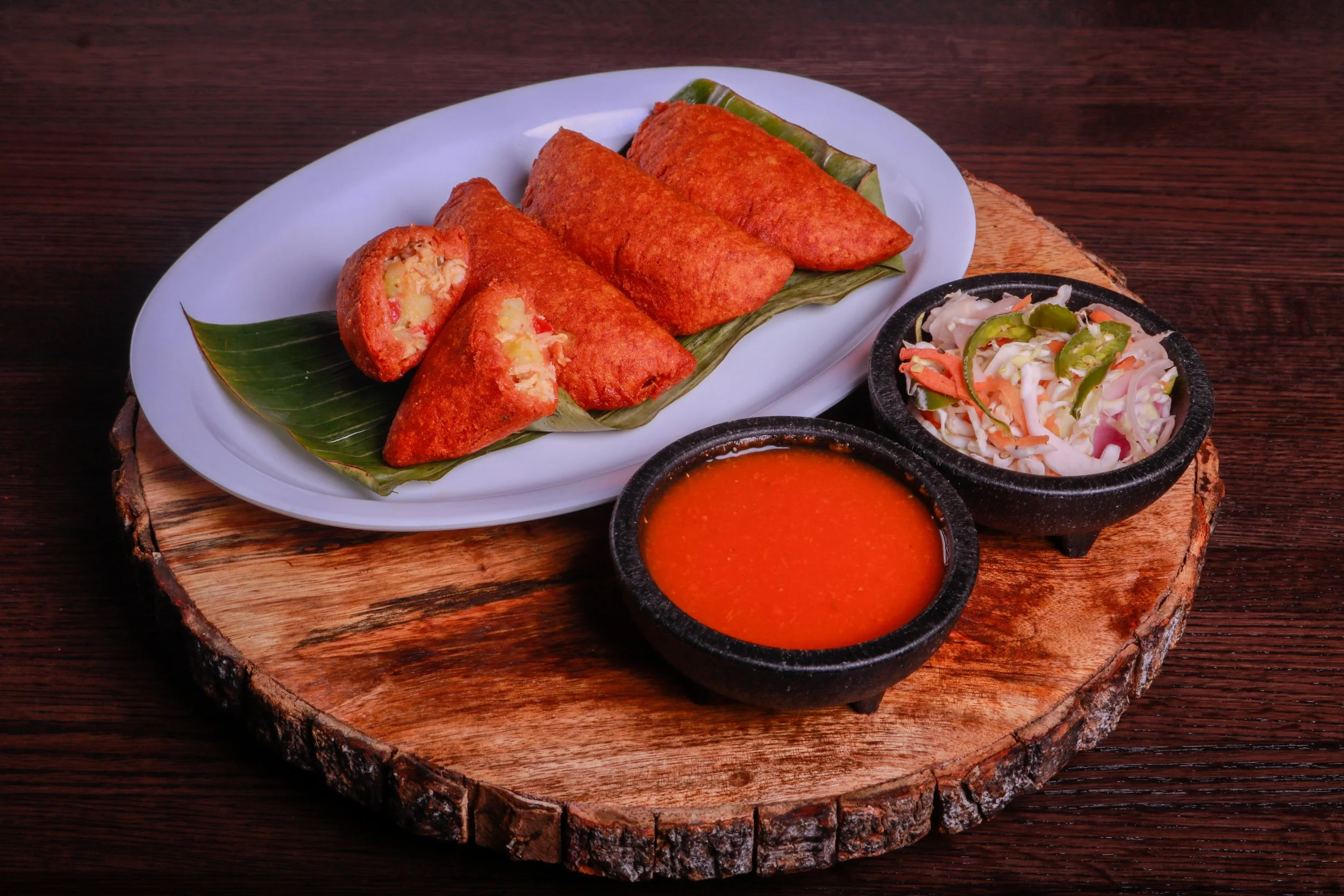 Crispy stuffed samosas served on a banana leaf with red dipping sauce and cabbage-carrot salad