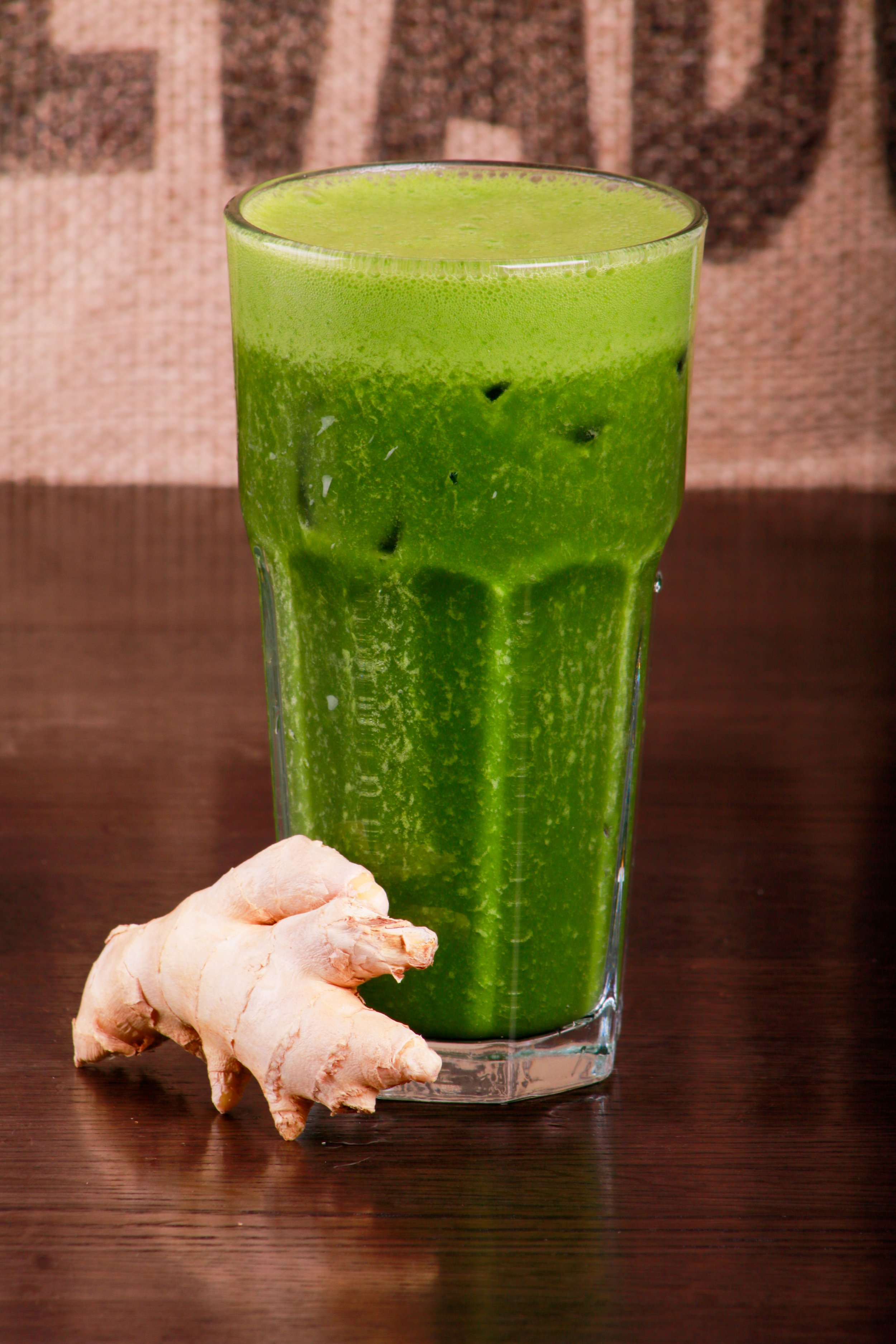 Glass of green juice with fresh ginger root on a wooden table
