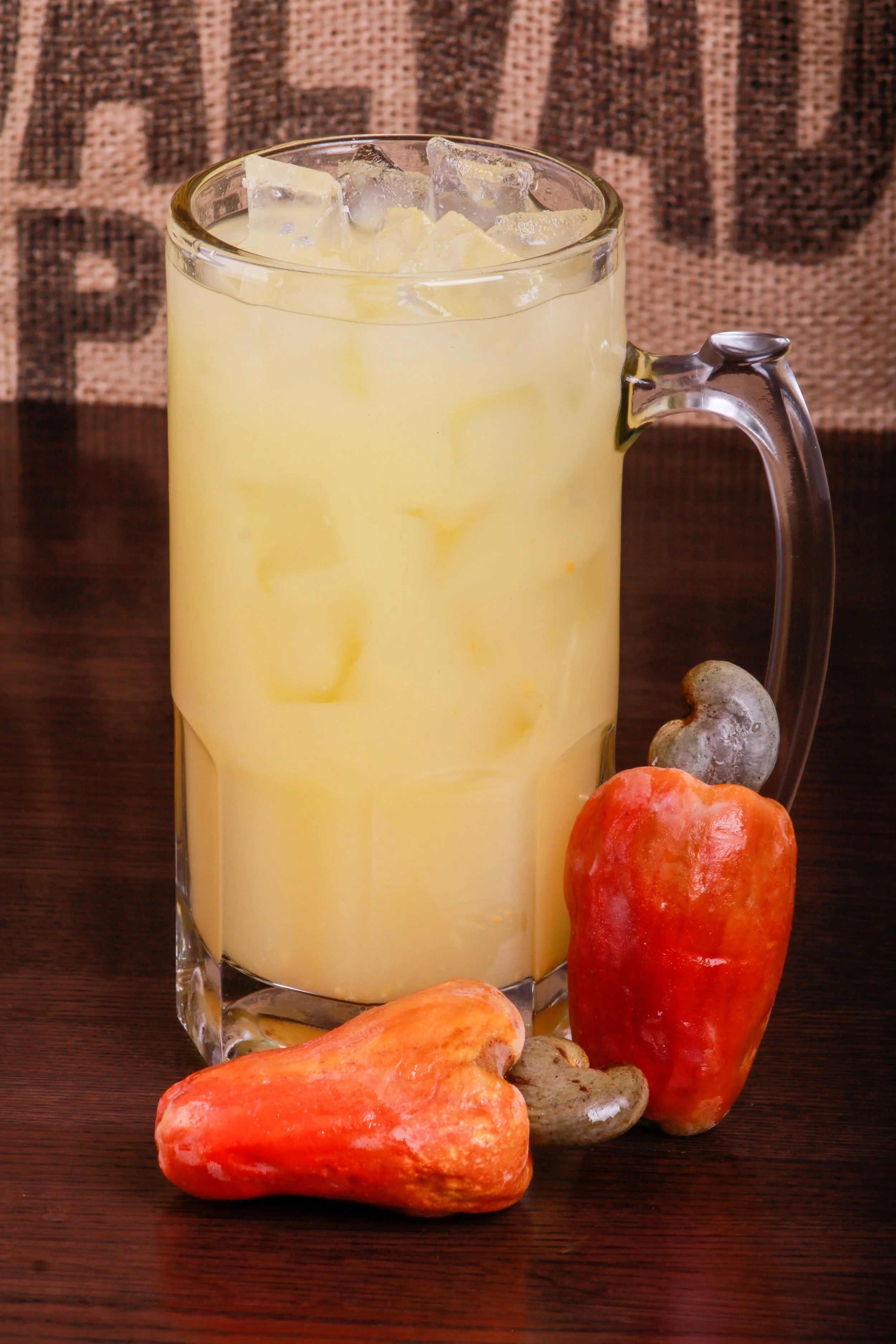Glass mug of pale yellow iced punch surrounded by colorful gourds on a wooden table