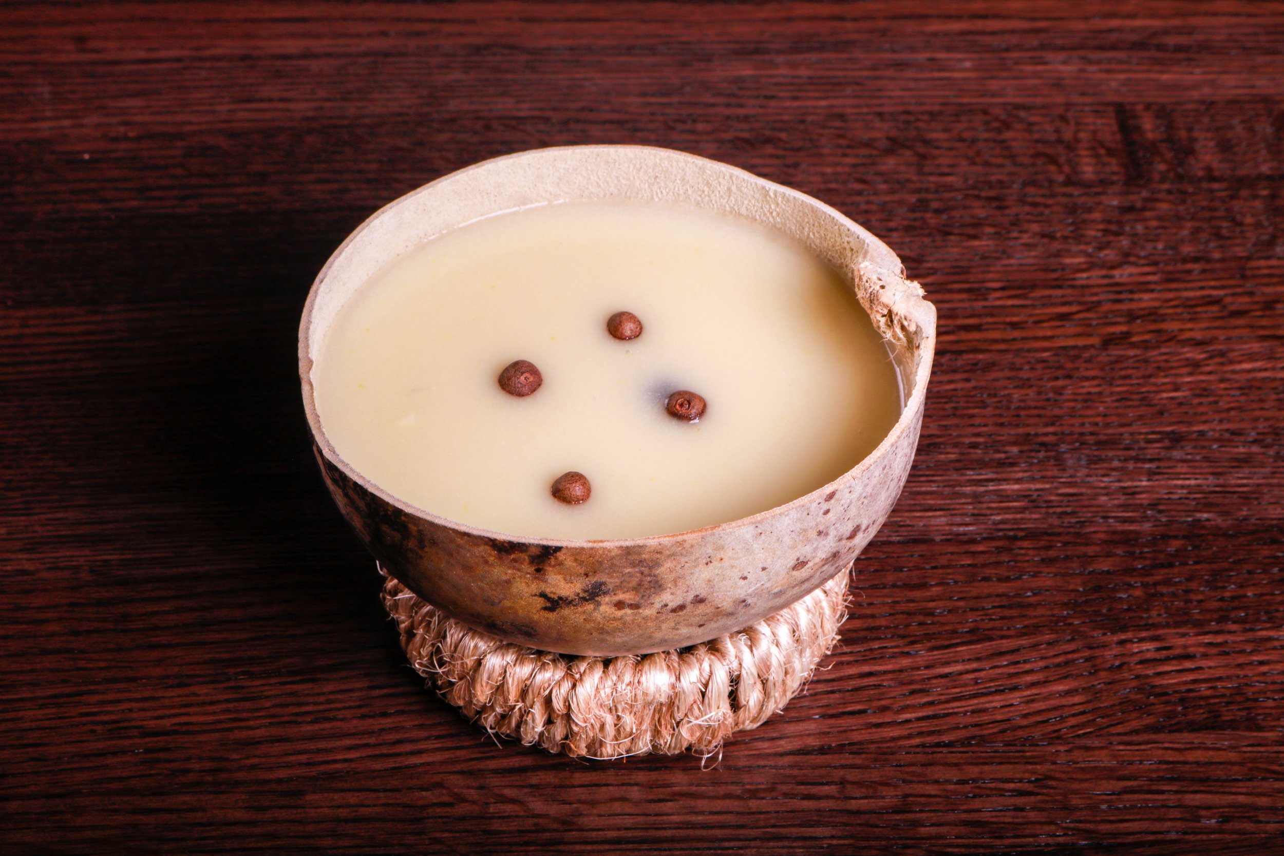Cream-colored coconut shell candle with coffee beans on a dark wooden table