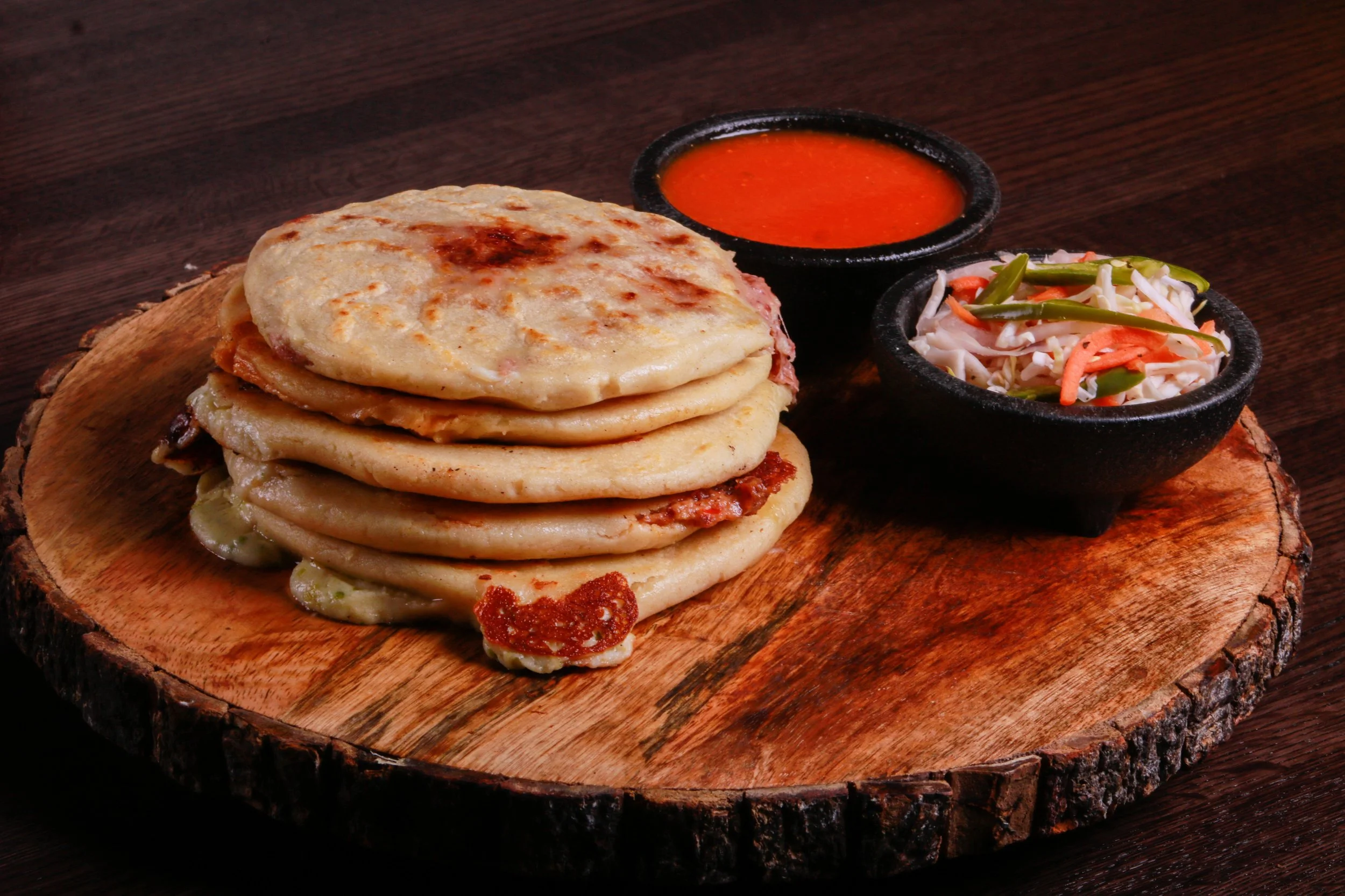 Stack of stuffed flatbreads served with red dipping sauce and shredded vegetable salad on a wooden board