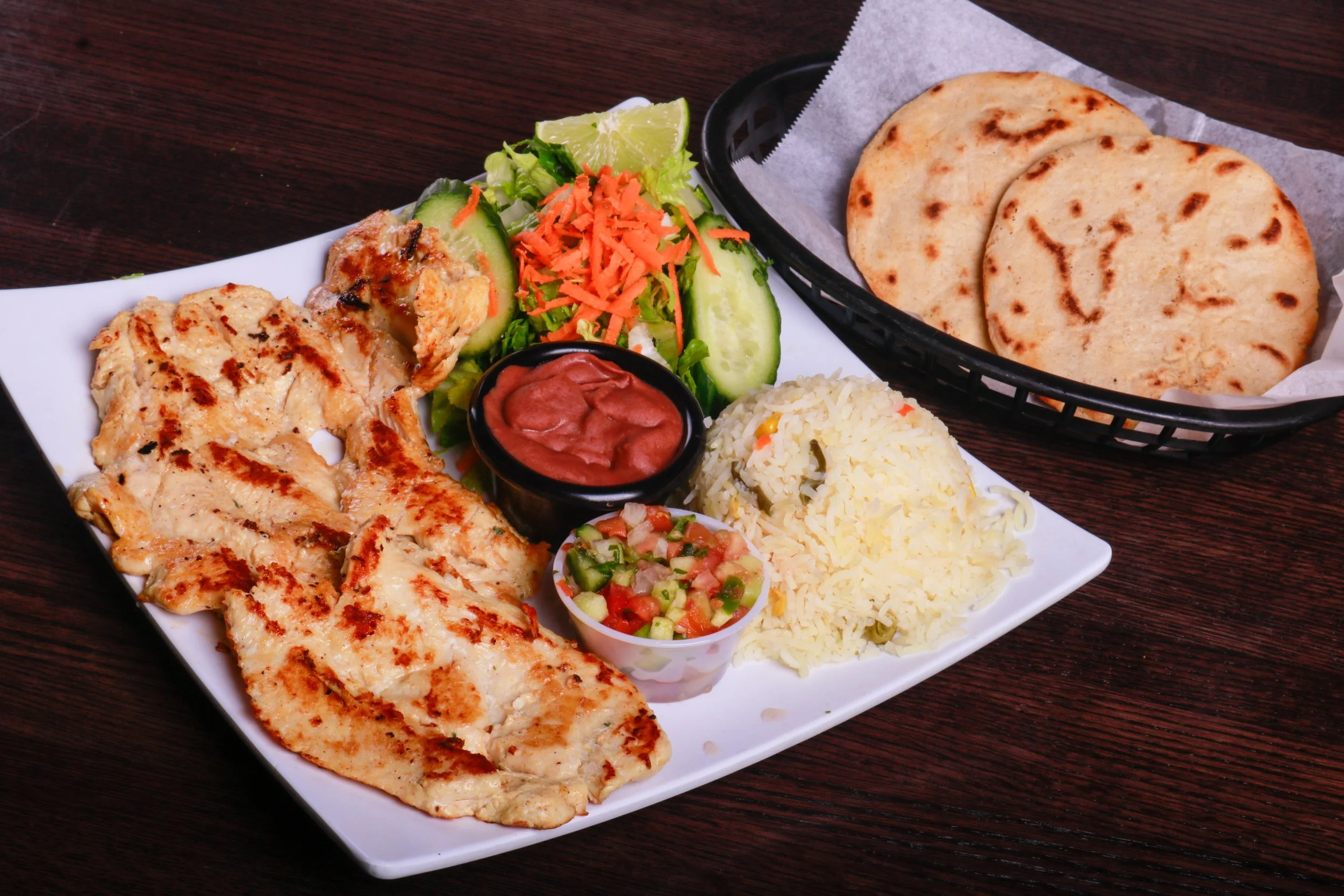 Grilled chicken platter with rice, salad, hummus, pico de gallo, lime, and flatbread