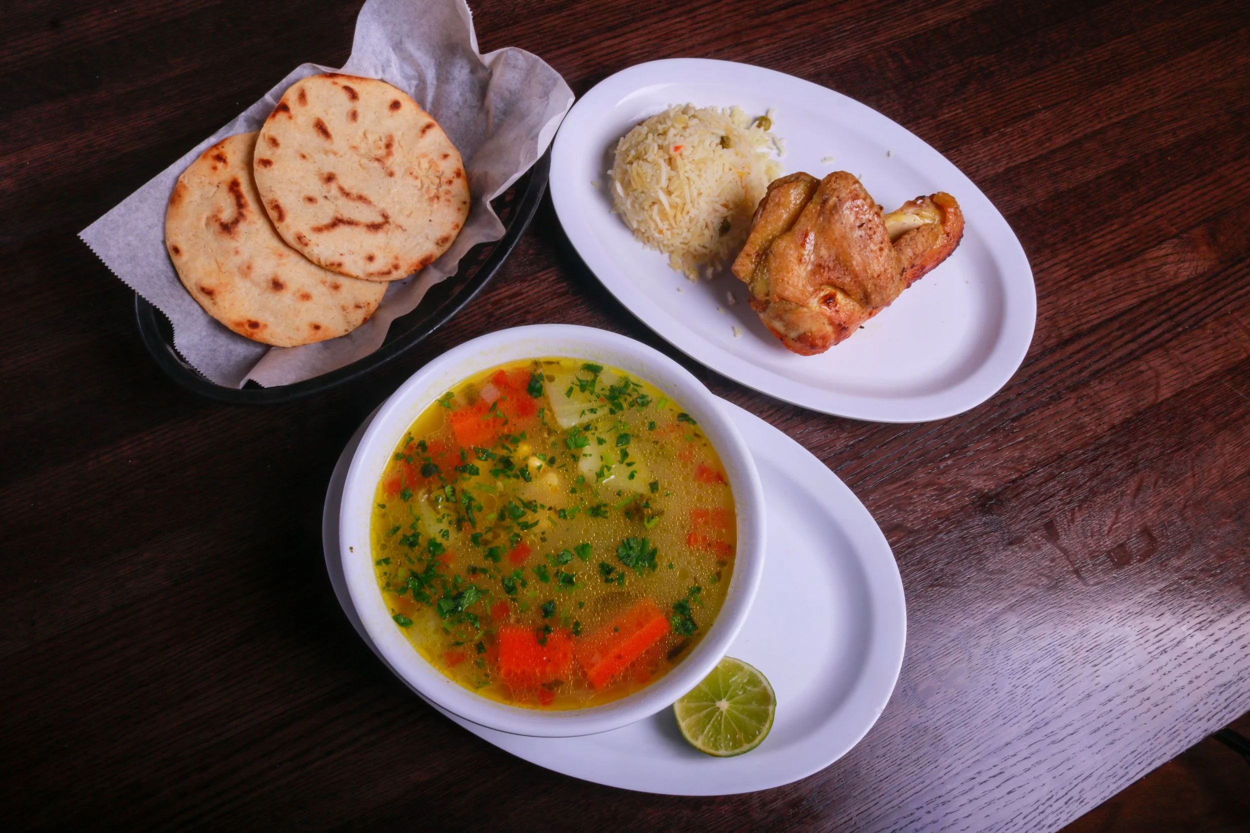 Latin American meal with grilled chicken, seasoned rice, vegetable soup, tortillas, and lime