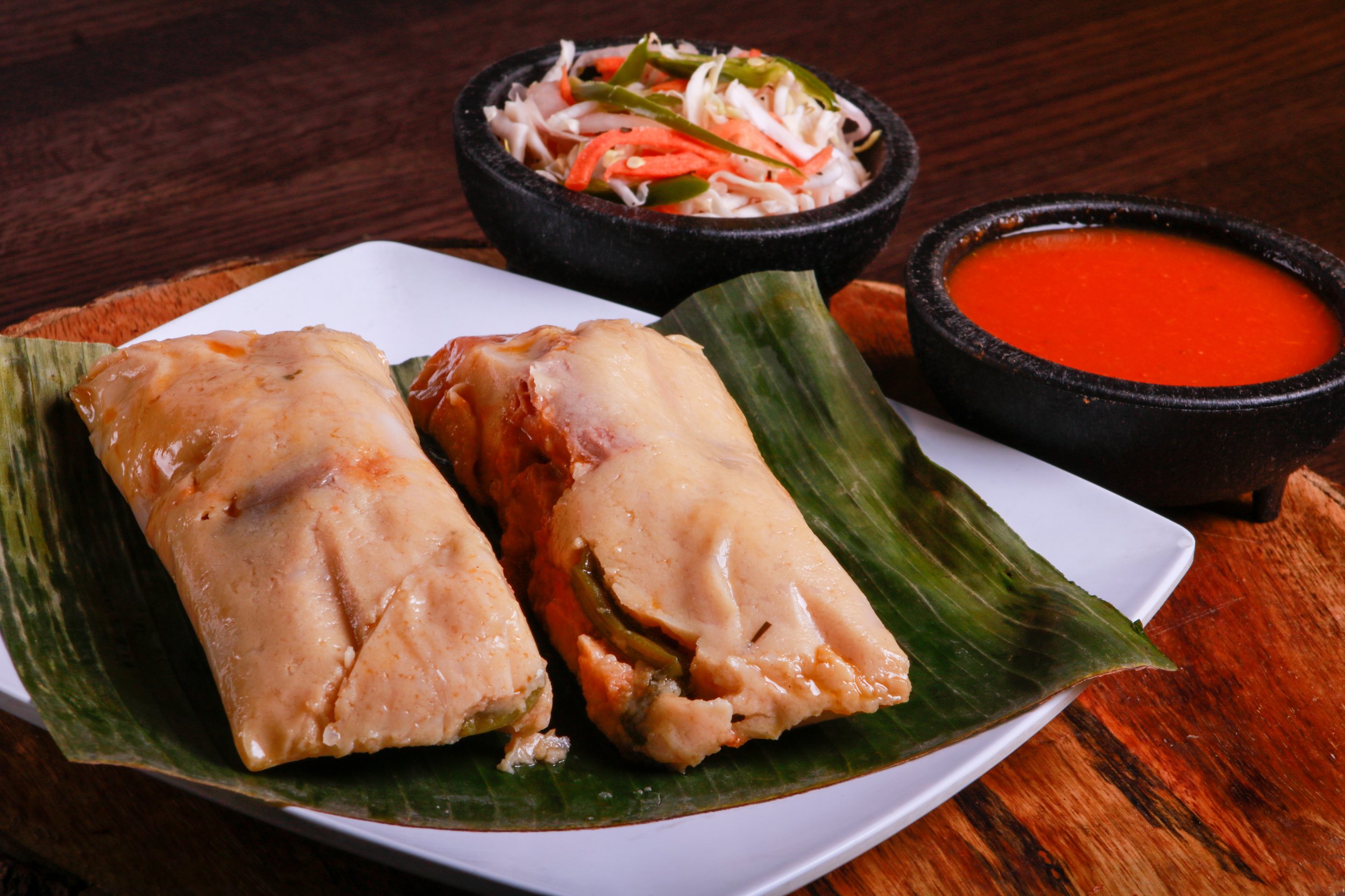 Steamed chicken tamales served on a banana leaf with cabbage slaw and red salsa