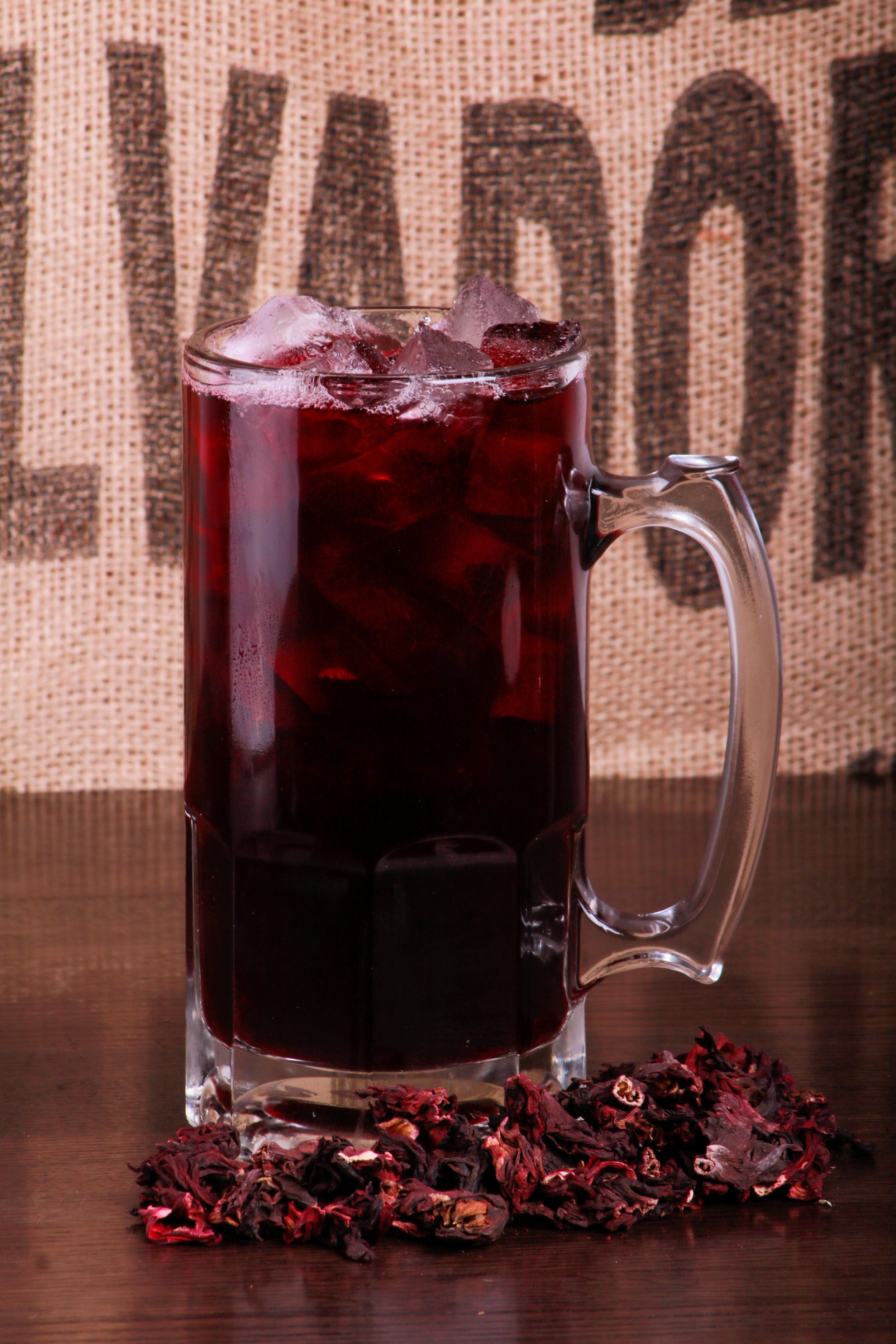 Glass pitcher of dark red hibiscus tea with ice, surrounded by dried hibiscus flowers