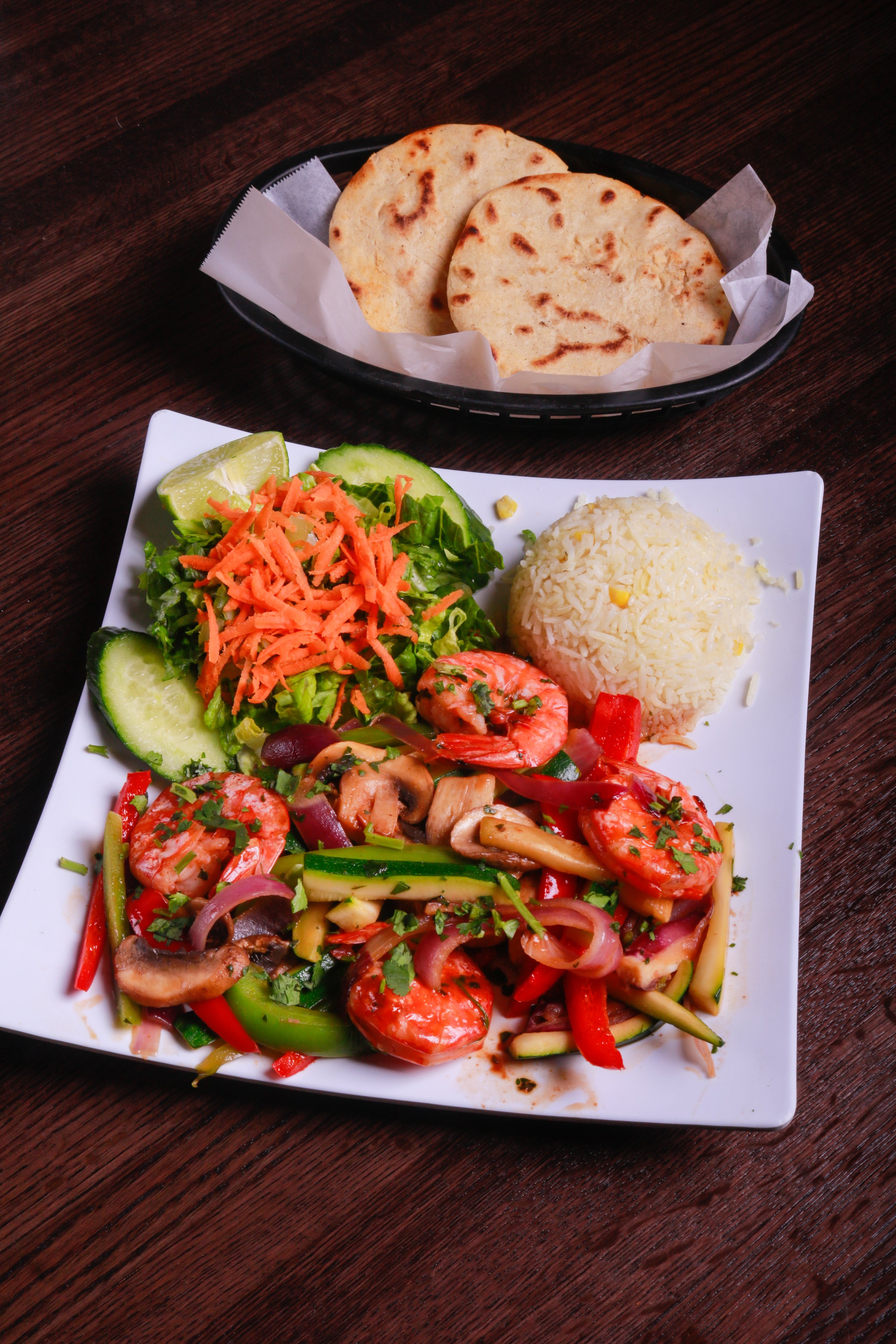 Shrimp and sautéed vegetables with rice, salad, lime, and flatbread on a restaurant table