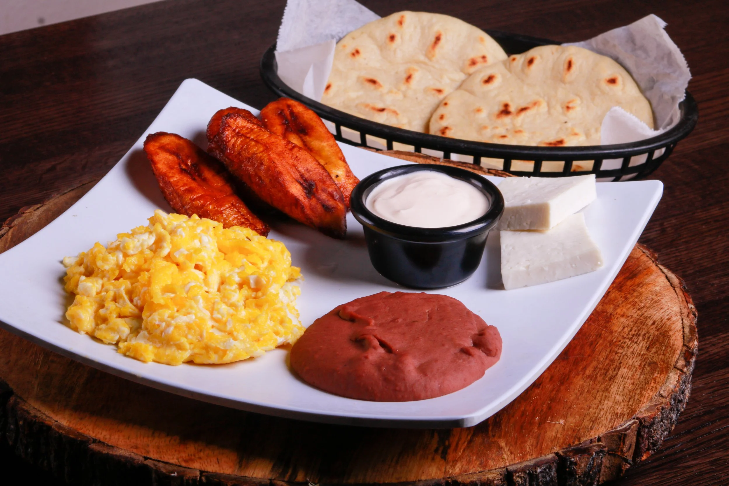 Traditional breakfast platter with scrambled eggs, fried plantains, cheese, red sausage, cream sauce, and flatbread