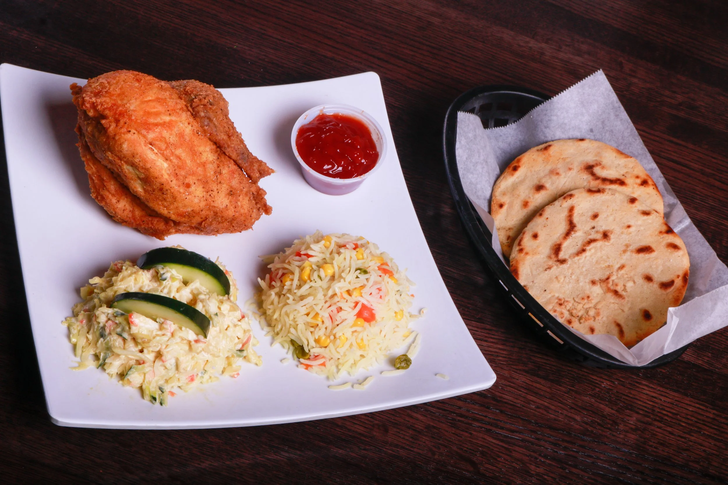 Platter of fried chicken with ketchup, vegetable rice, creamy salad, and cucumber, served with grilled flatbreads.