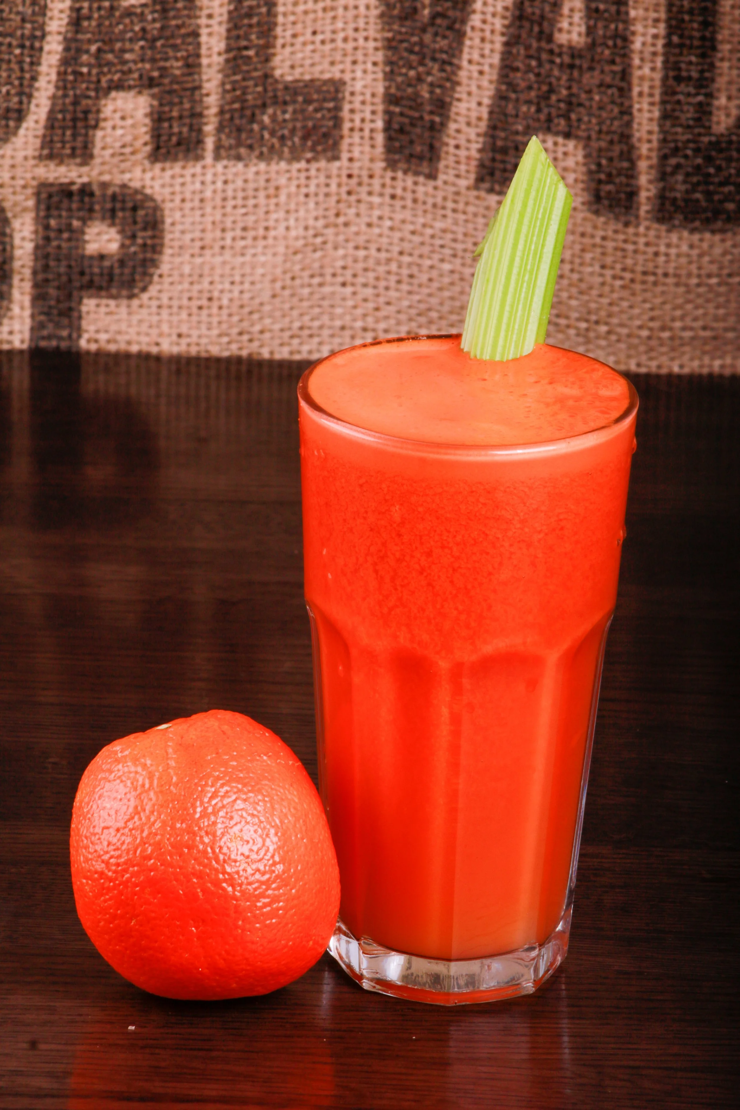 Glass of orange juice with a celery stick garnish beside a whole orange on a wooden table