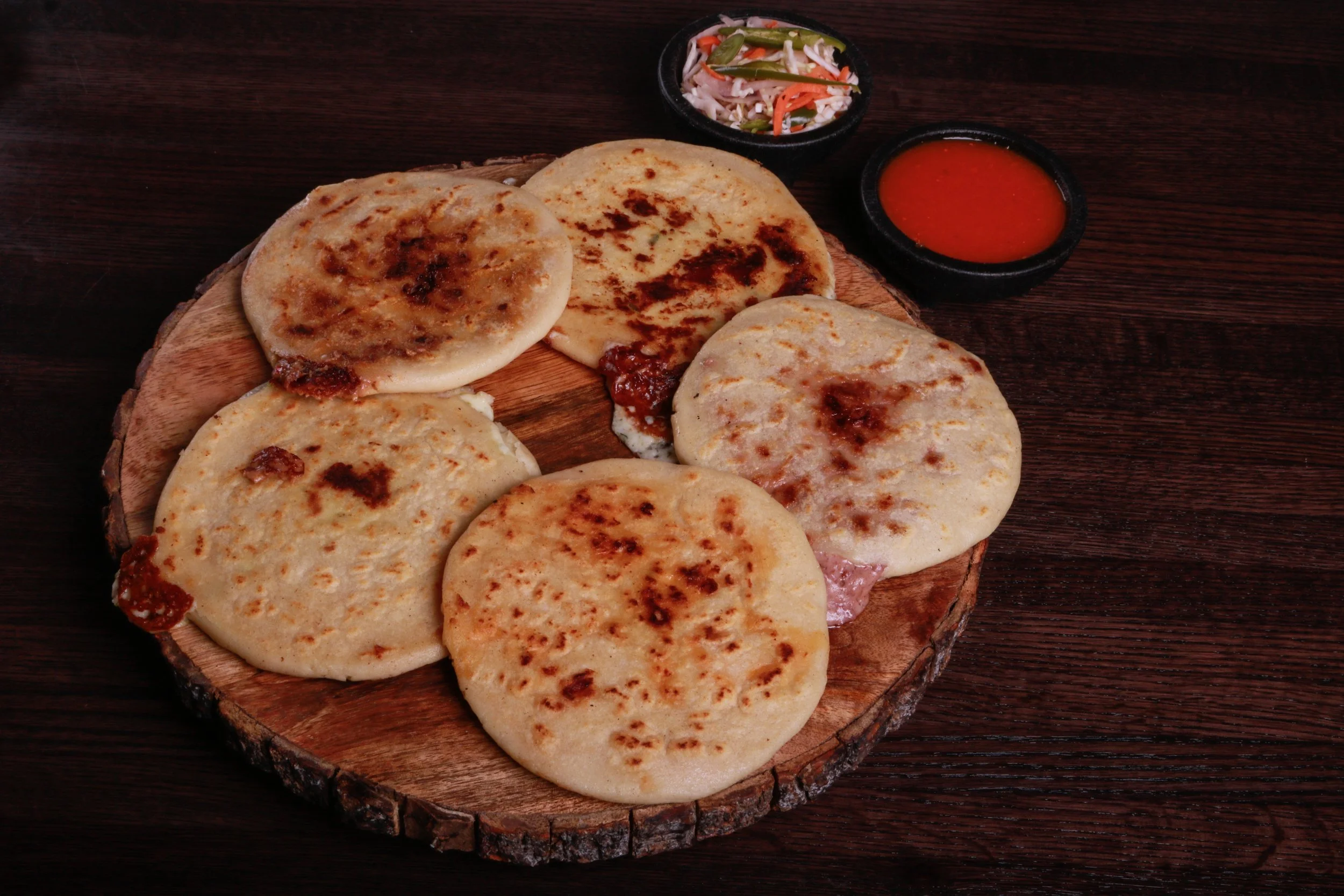 Grilled stuffed flatbreads served on a wooden board with red dipping sauce and pickled vegetables