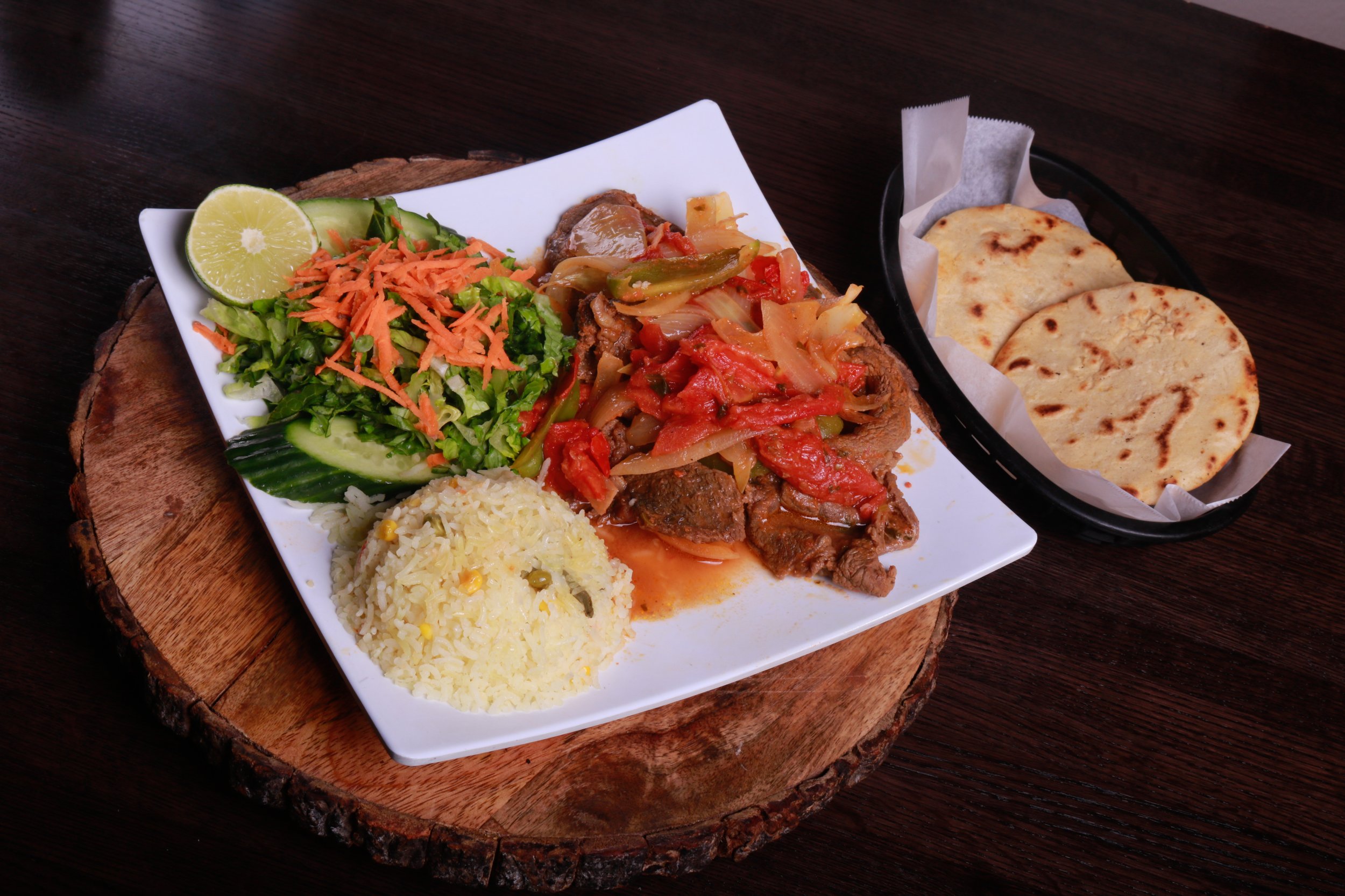Latin American steak platter with sautéed onions and peppers, rice, salad, lime, and flatbread