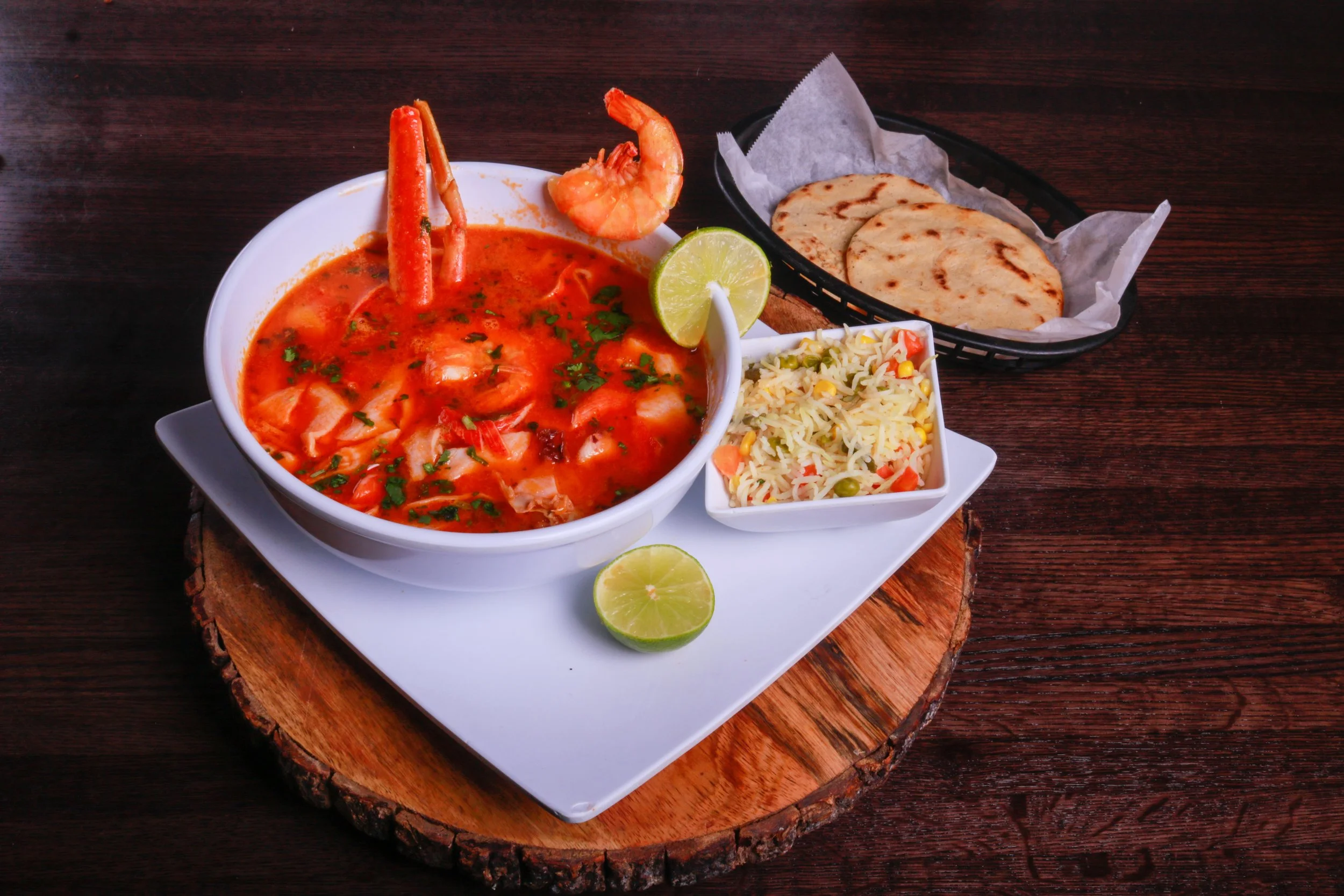 Seafood stew with shrimp and crab, vegetable rice, grilled flatbread, and lime wedges