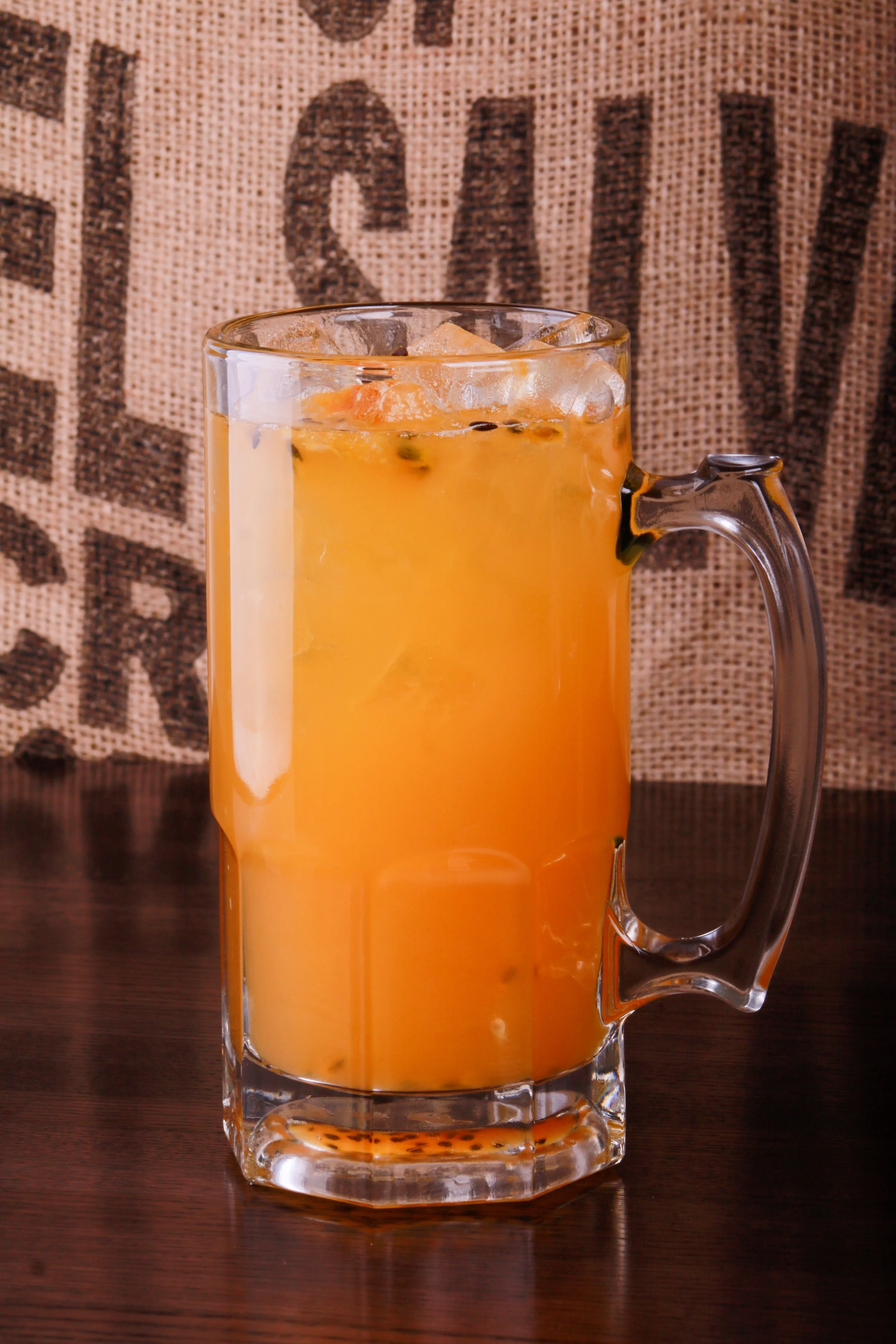 Glass mug of orange passion fruit juice with ice on a wooden table