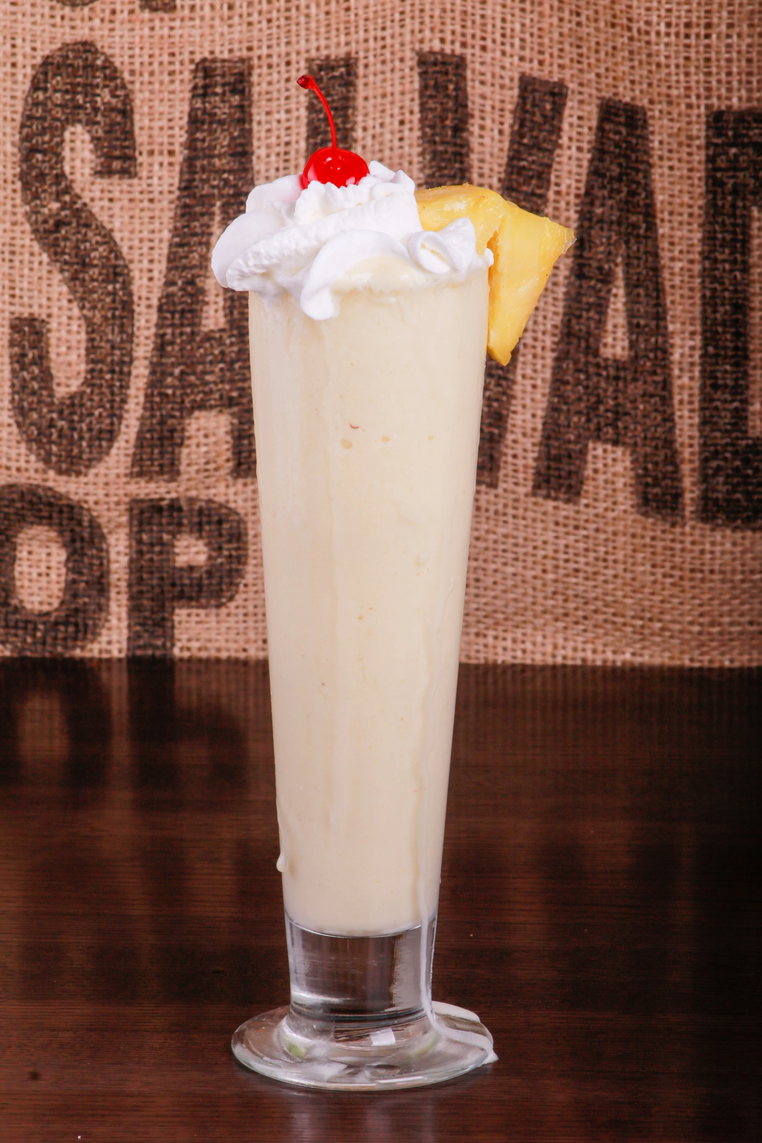 Creamy pineapple smoothie topped with whipped cream and a maraschino cherry in a glass with a pineapple wedge
