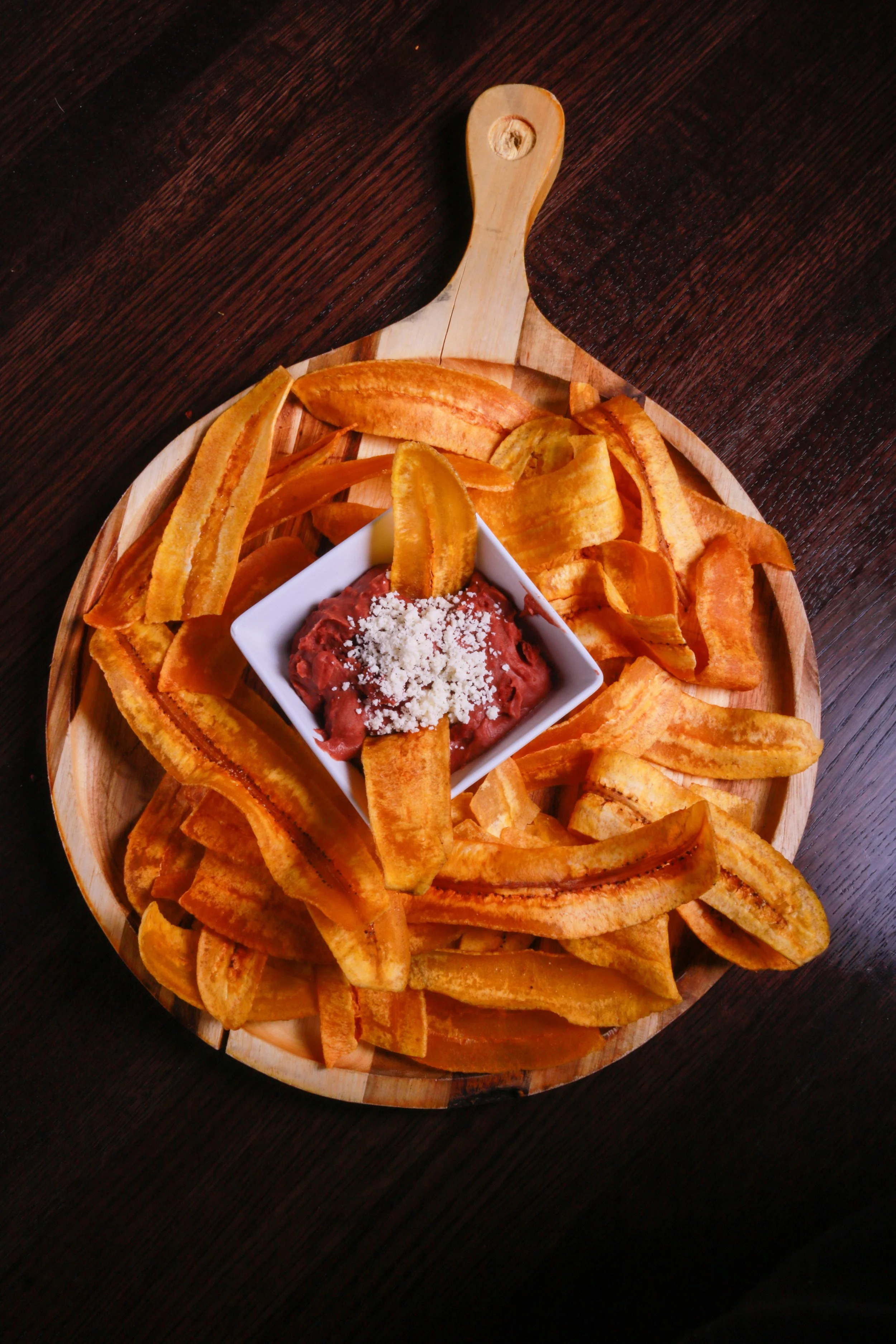 Wooden serving platter of tortilla chips with red bean dip topped with crumbled cheese