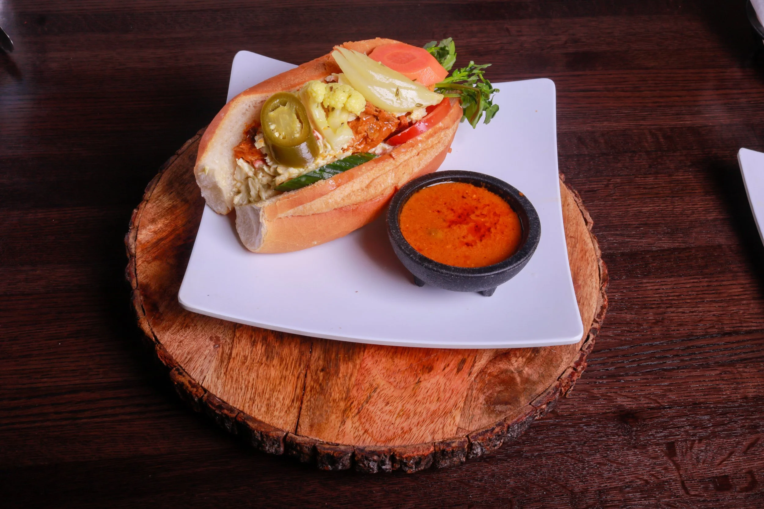 Loaded sandwich with chicken, pickled vegetables, jalapeños, tomato, cucumber, and greens served with orange dipping sauce