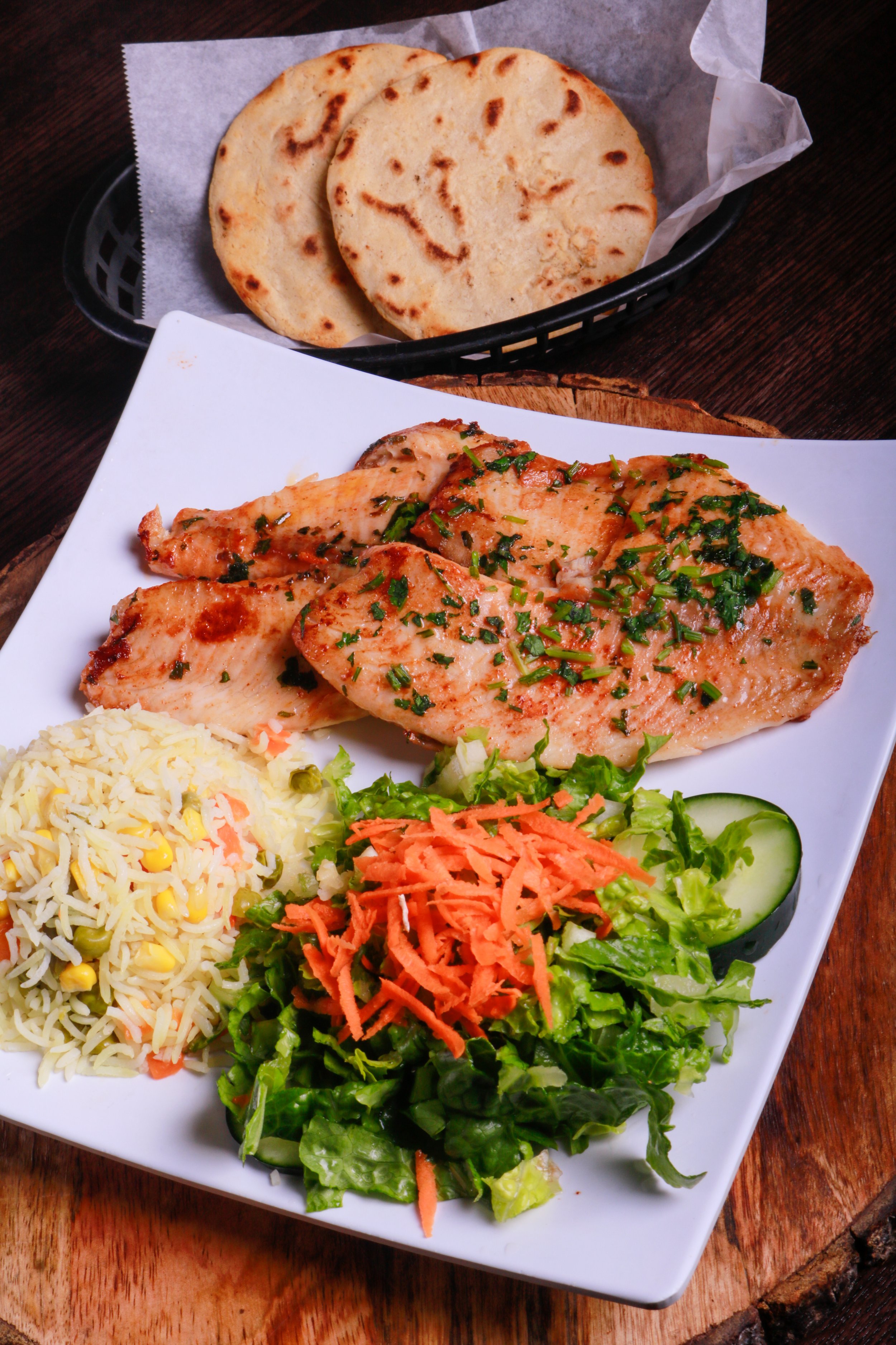 Grilled herb-seasoned chicken served with vegetable rice, lettuce salad, shredded carrots, cucumber, and flatbread.