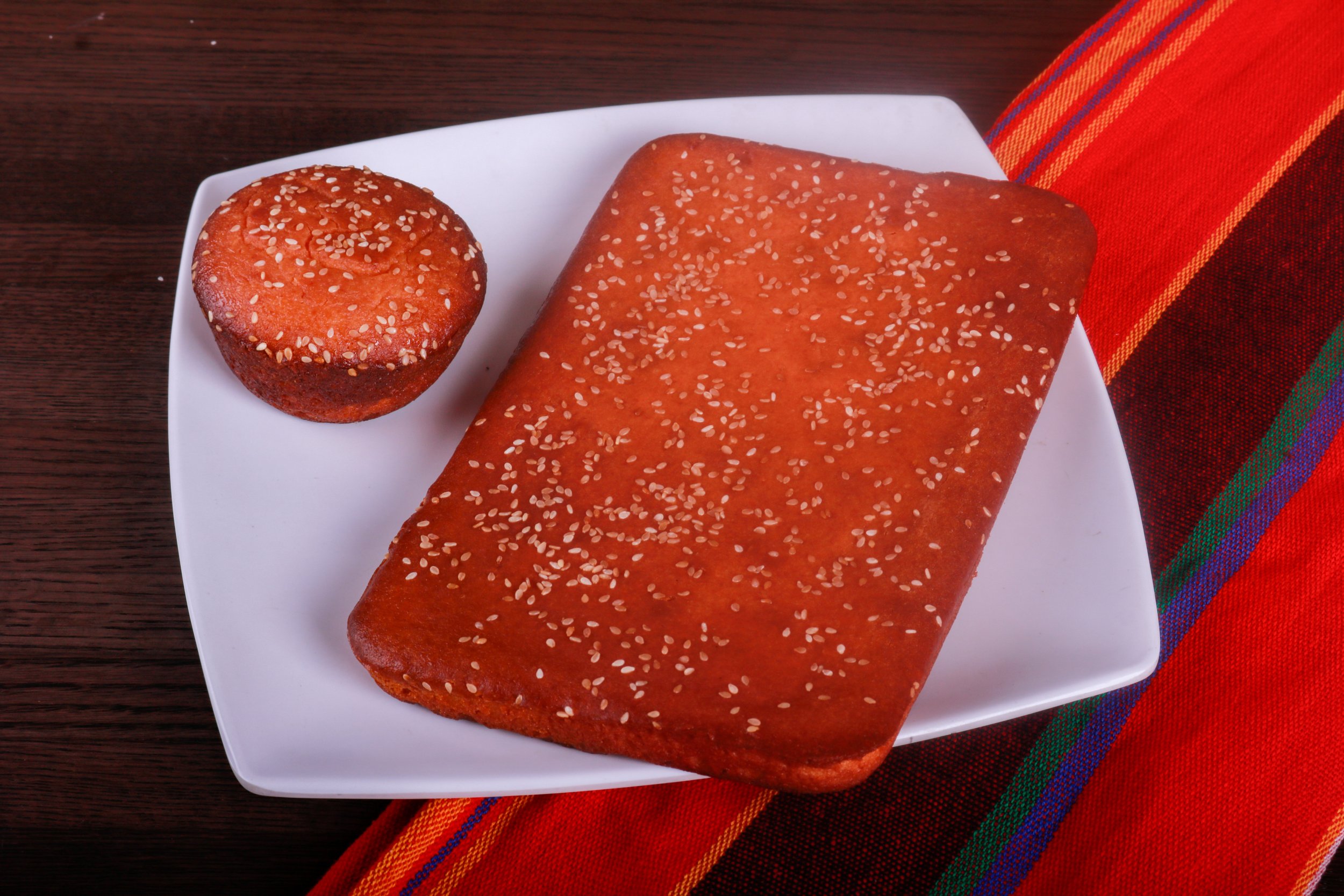 Sesame-seed bread loaf and roll on a white plate with a colorful striped napkin