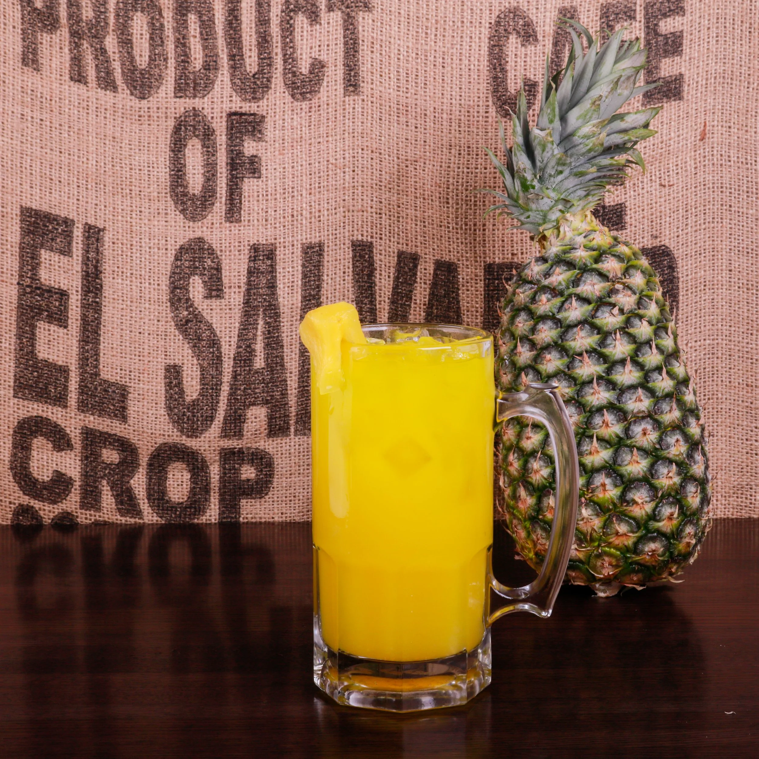 Glass of pineapple juice with a pineapple garnish beside a whole pineapple on a wooden table