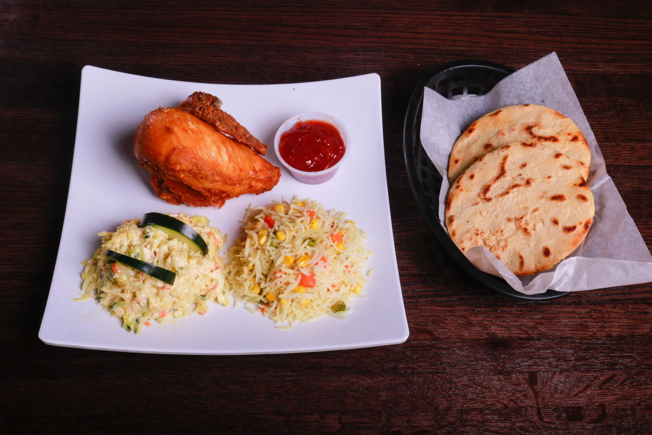 Plate of fried chicken with ketchup, vegetable rice, and creamy coleslaw, served with grilled flatbreads.