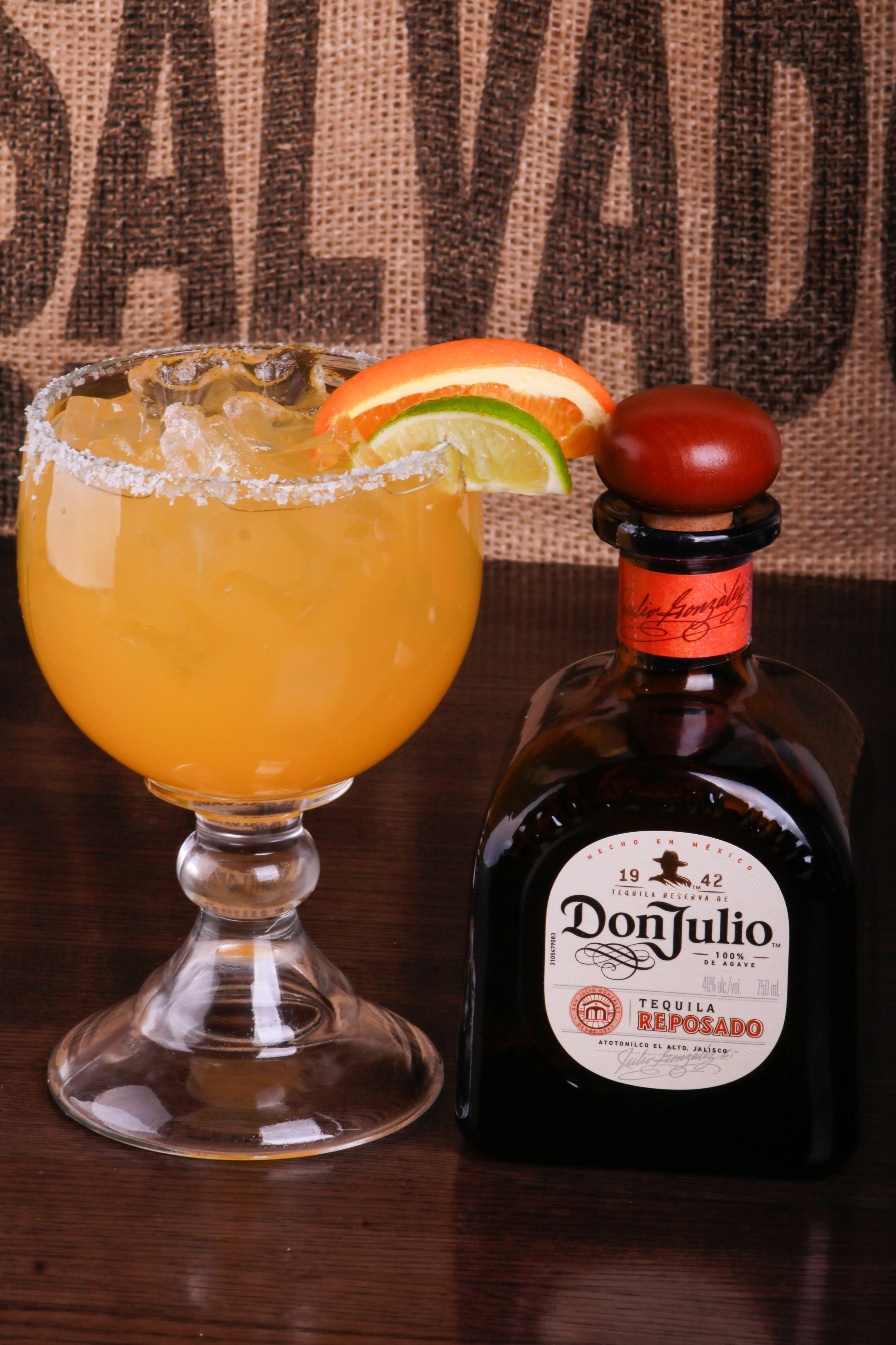Salt-rimmed citrus cocktail with lime and orange garnishes beside a Don Julio Reposado tequila bottle