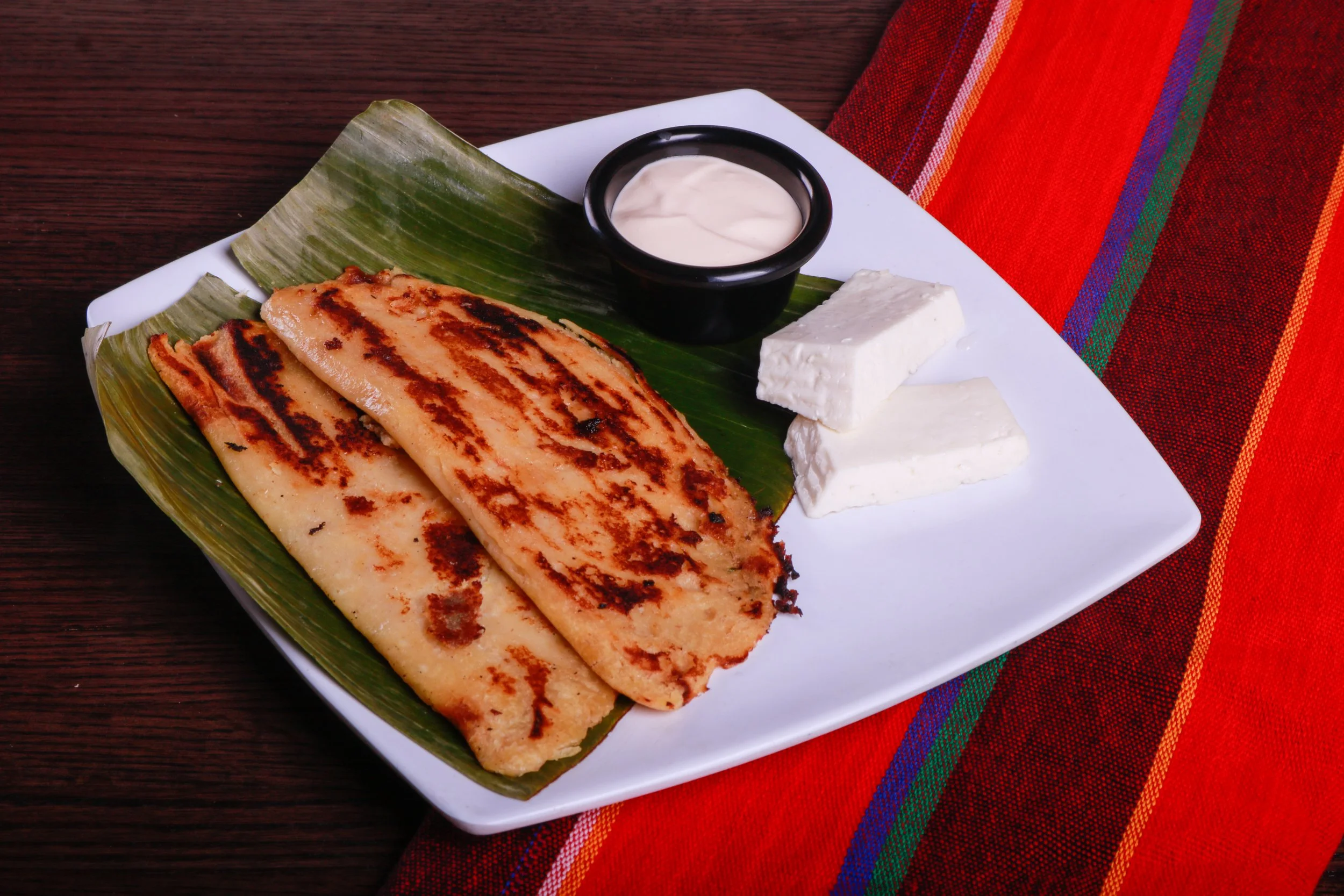 Grilled Colombian arepas served on a banana leaf with white cheese and creamy dipping sauce