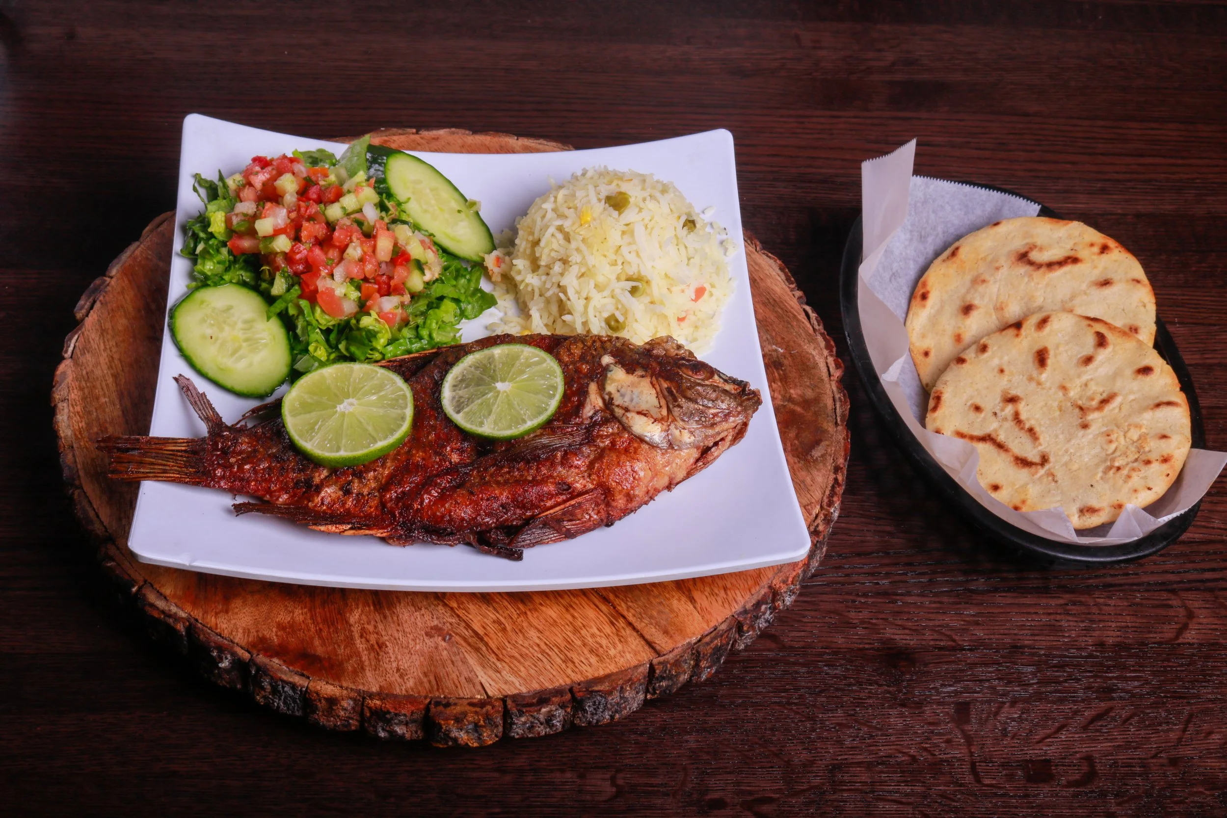 Grilled whole fish with lime, rice, salad, and flatbread served on a platter