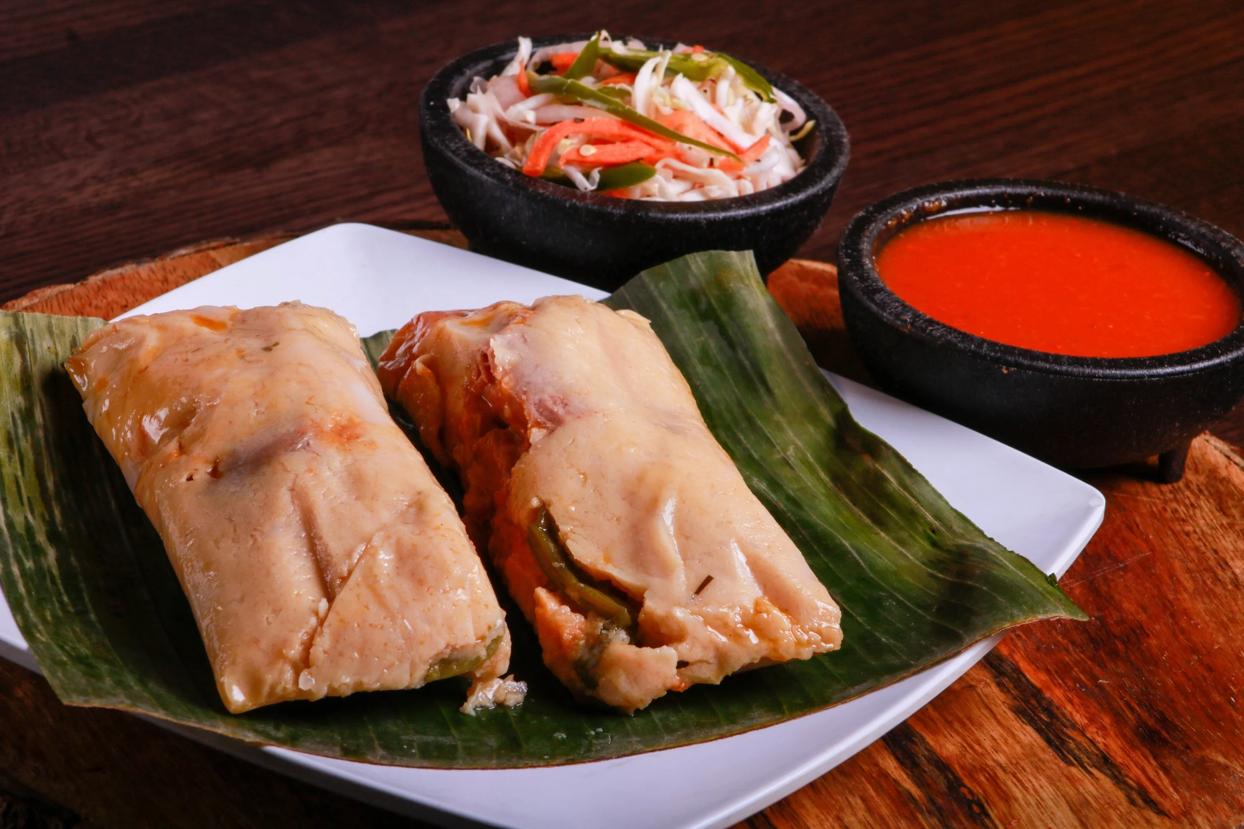 Steamed tamales served on a banana leaf with cabbage slaw and red salsa