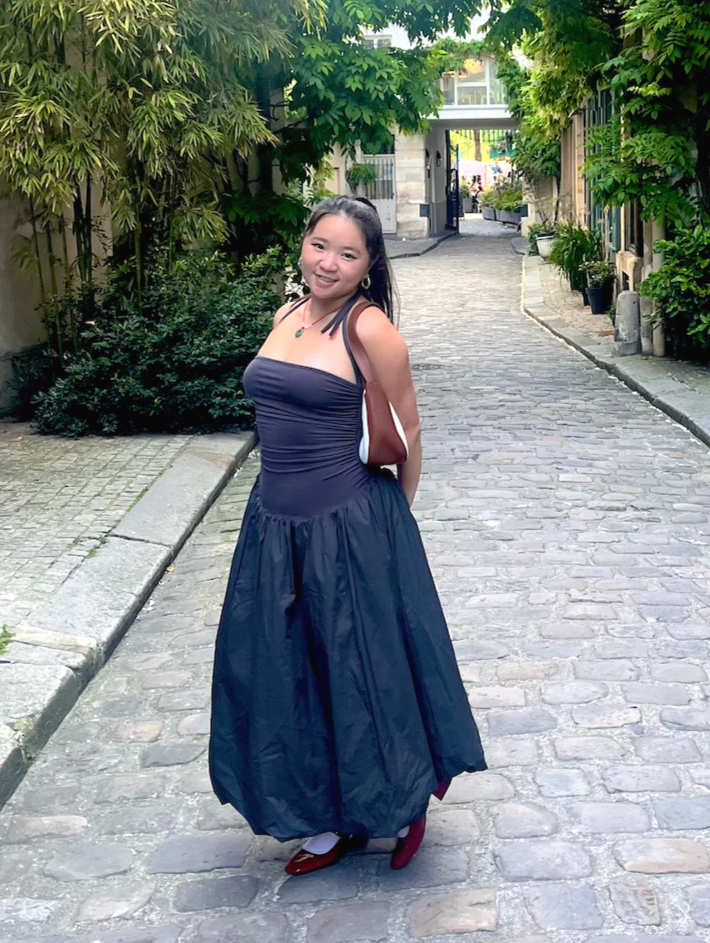 Woman in a dark blue dress standing on a leafy cobblestone street