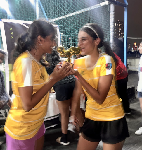 Two young women in yellow sports jerseys smiling and holding a trophy during a celebration event.