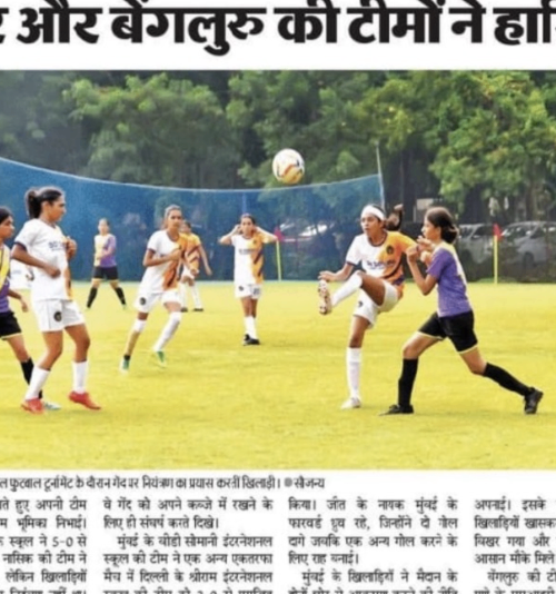 Women playing soccer outdoors on a green field with trees in the background, actively competing for the ball.