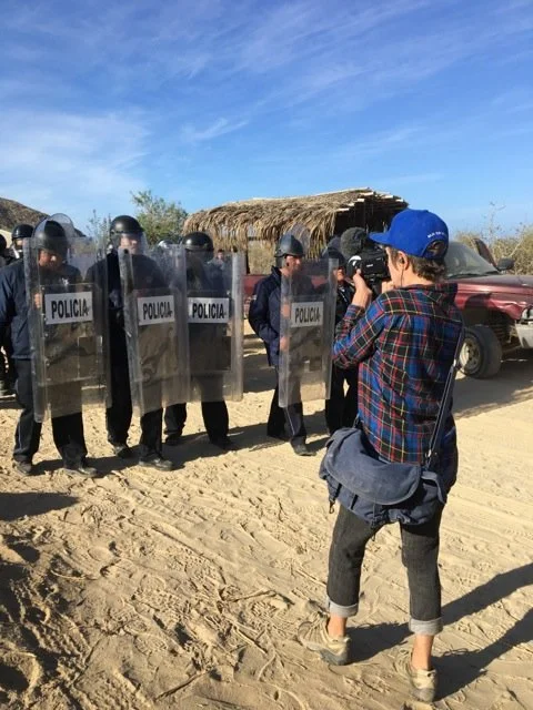 Photographer recording police officers with shields on a dirt road in a rural area.