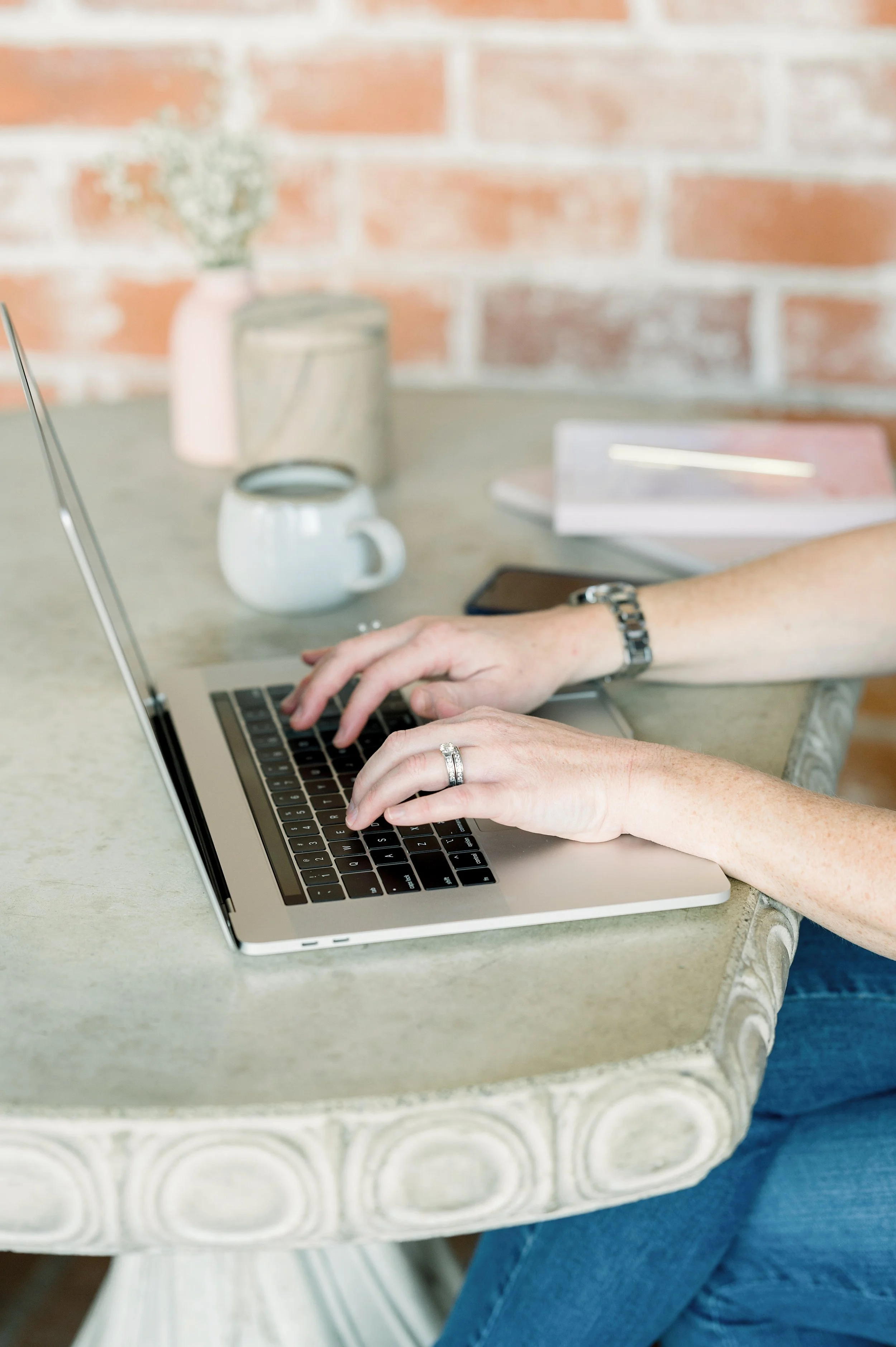 Person typing on a laptop at a desk with a coffee mug and smartphone nearby