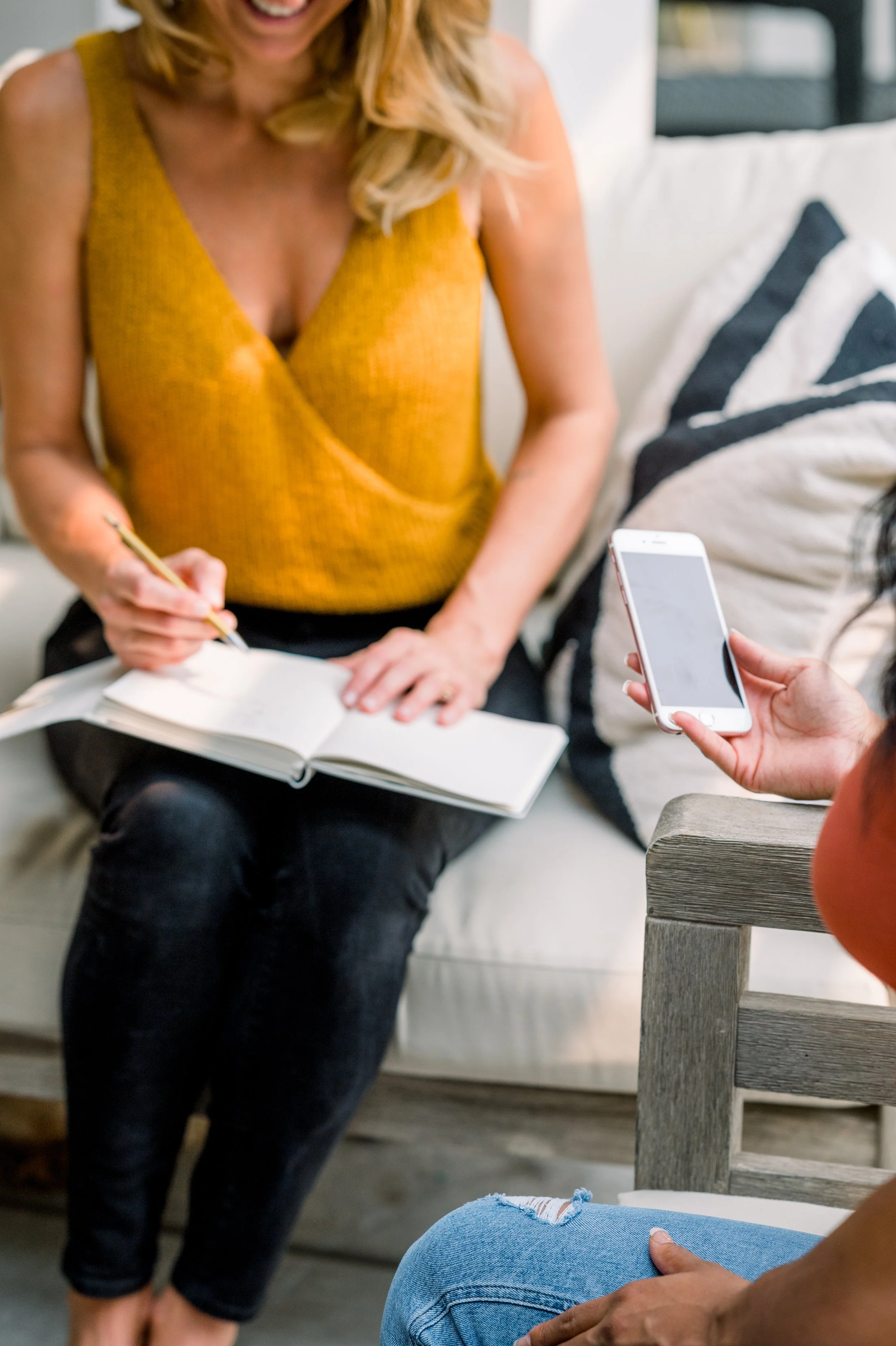 People collaborating indoors, with one person writing in a notebook and another holding a smartphone.