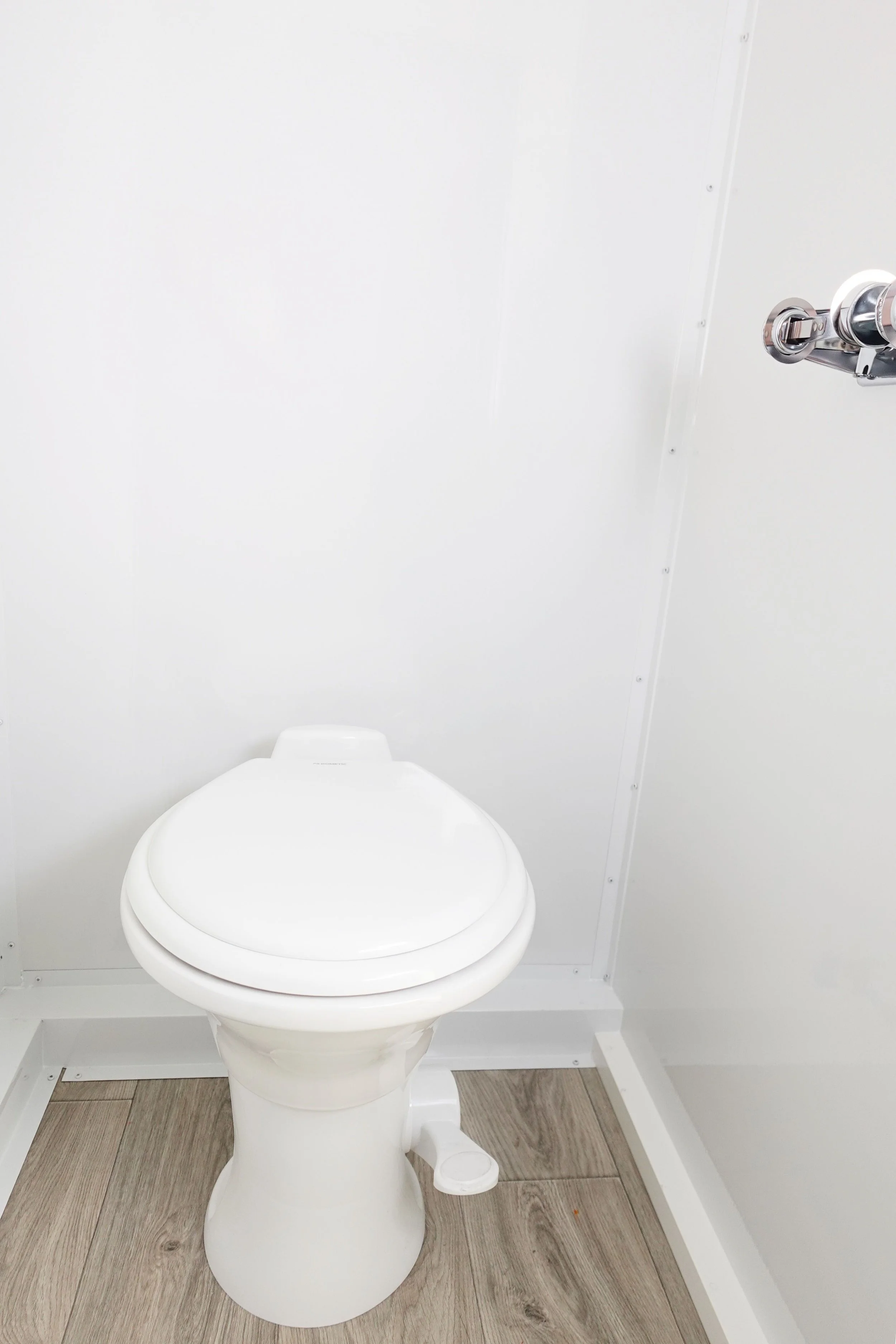 A white toilet in a small bathroom with white walls and gray wooden flooring.