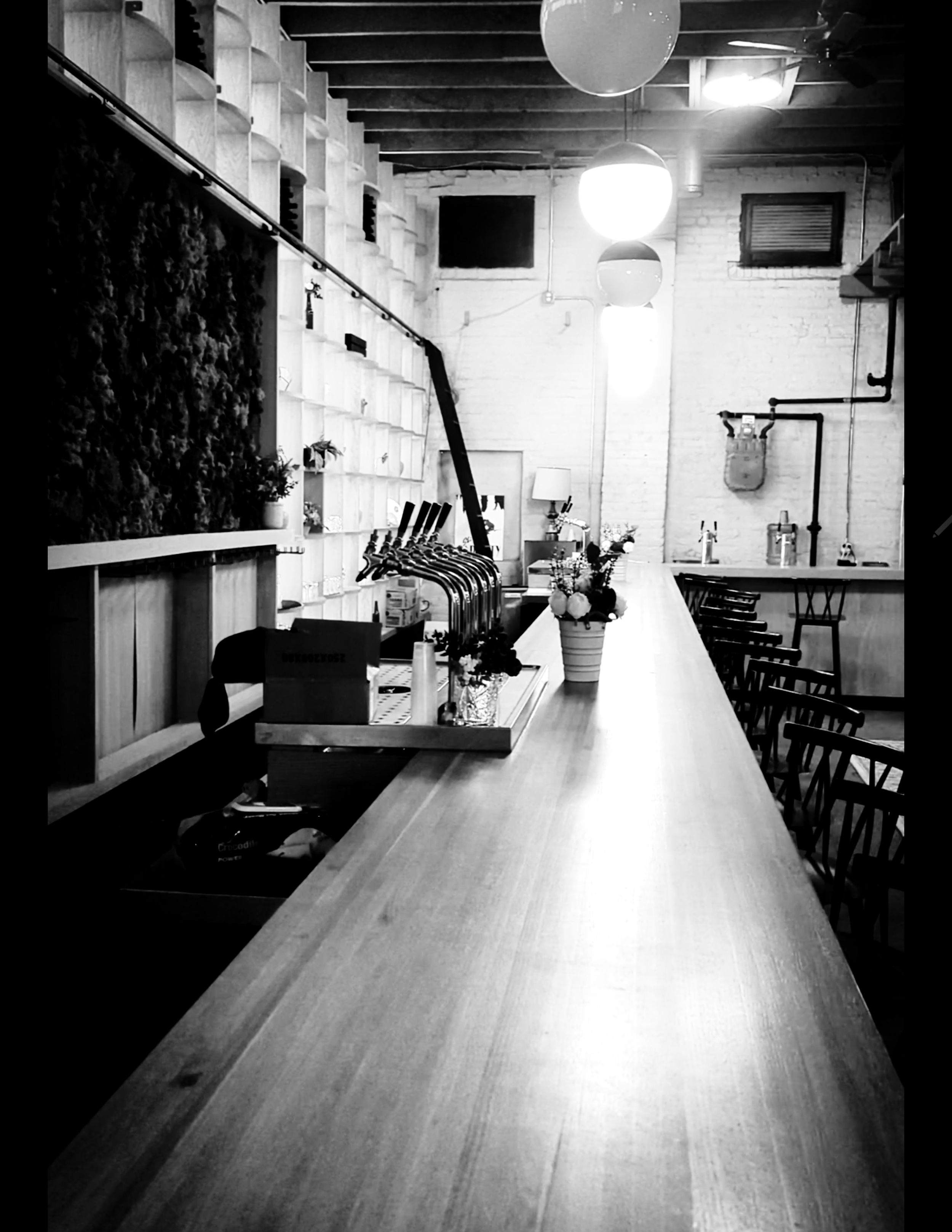 Black-and-white interior photograph showing a long counter, seating and hanging globe lights