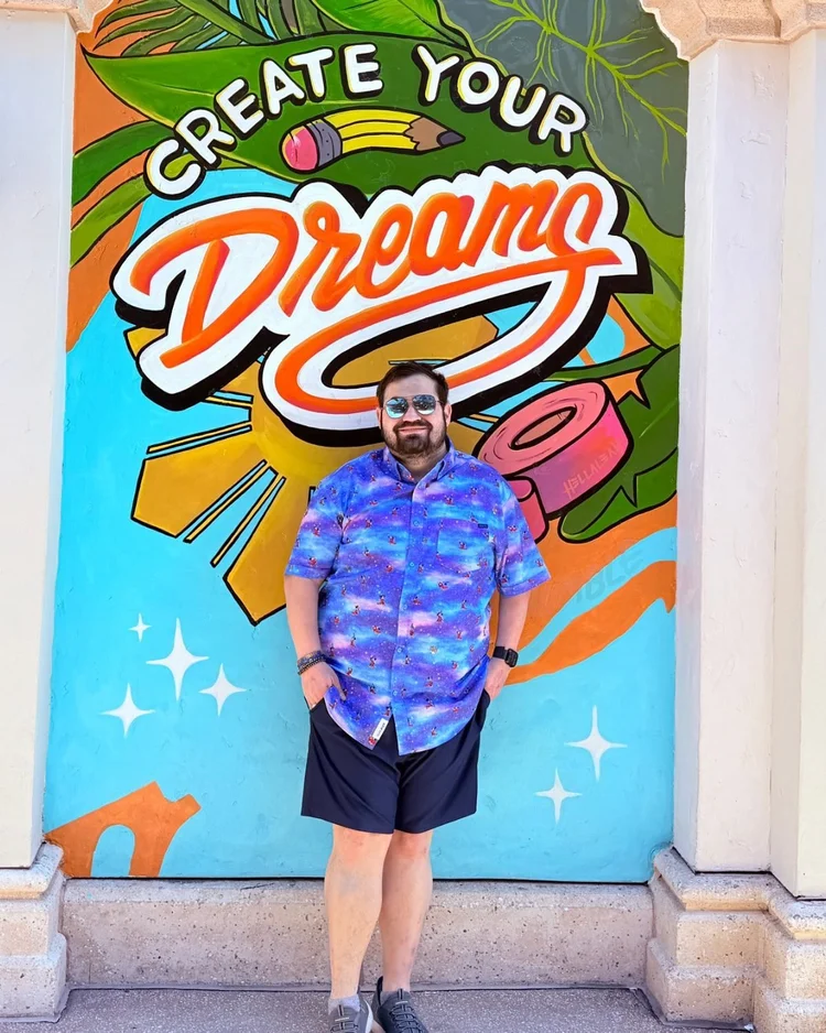 Josh standing in front of a colorful mural that reads Create Your Dreams