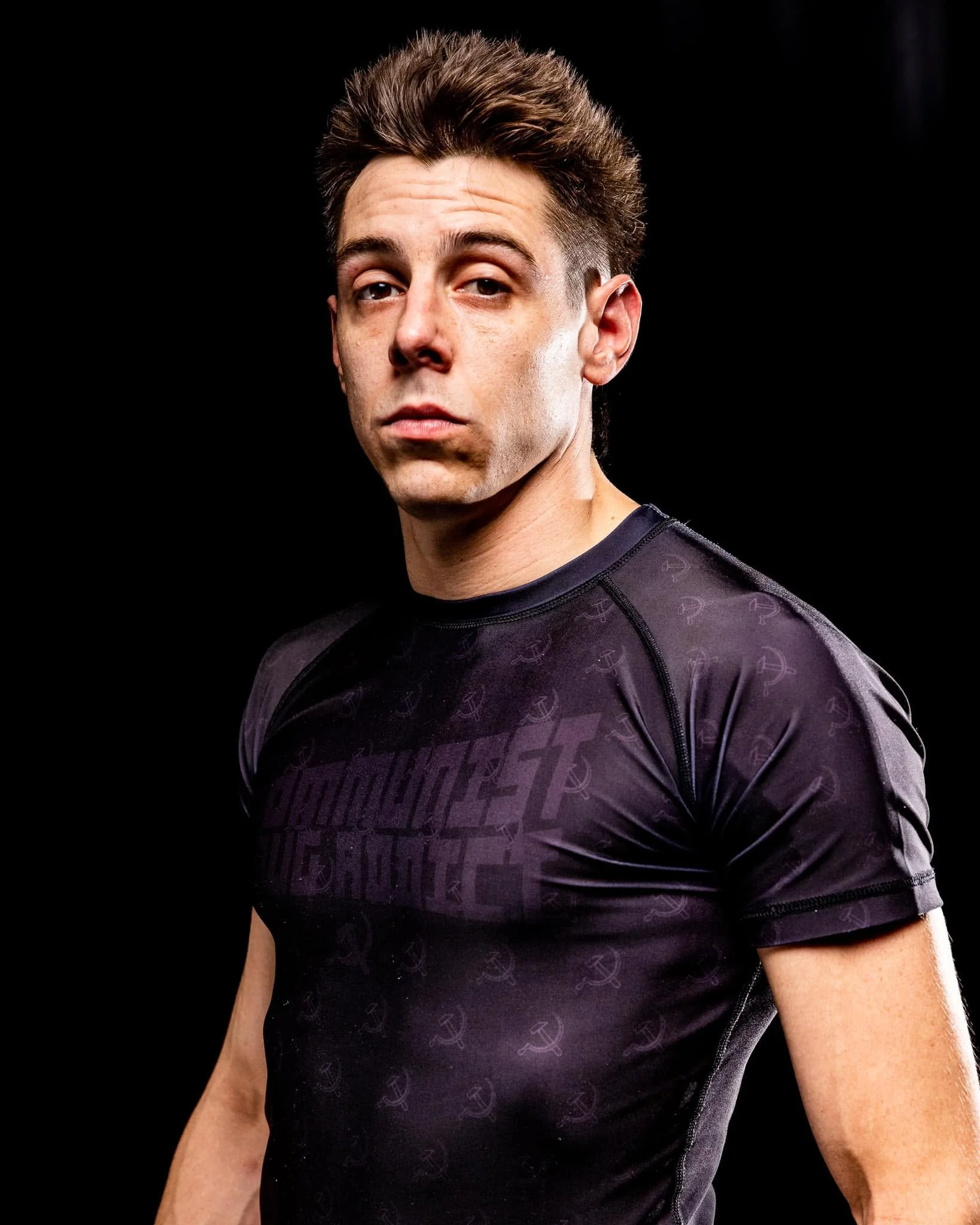 Close-up photo of a man with brown hair wearing a black athletic shirt against a black background.