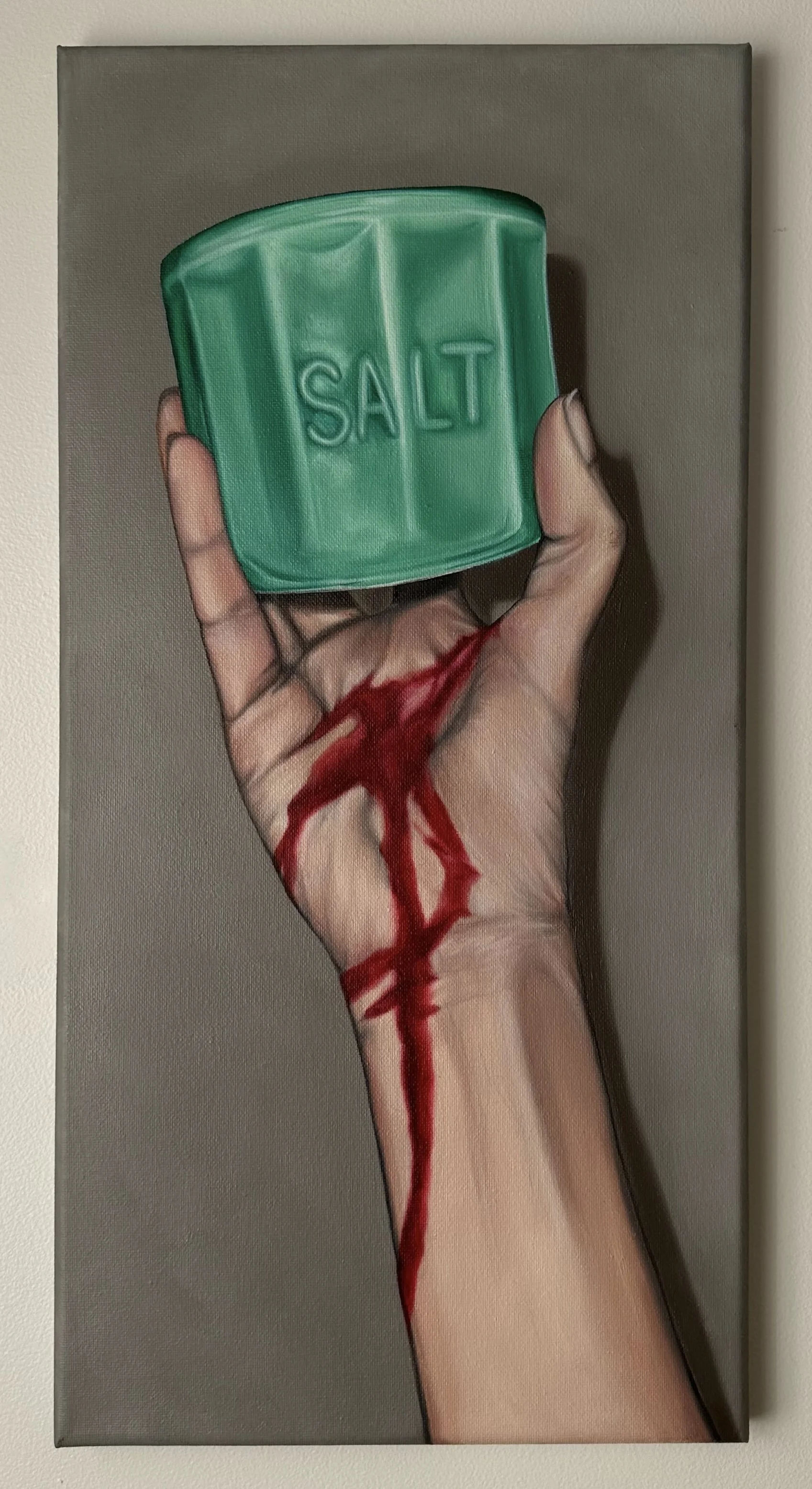 A painting of a hand holding a green salt cellar with the word 'SALT' embossed on it. The hand appears to be bleeding.