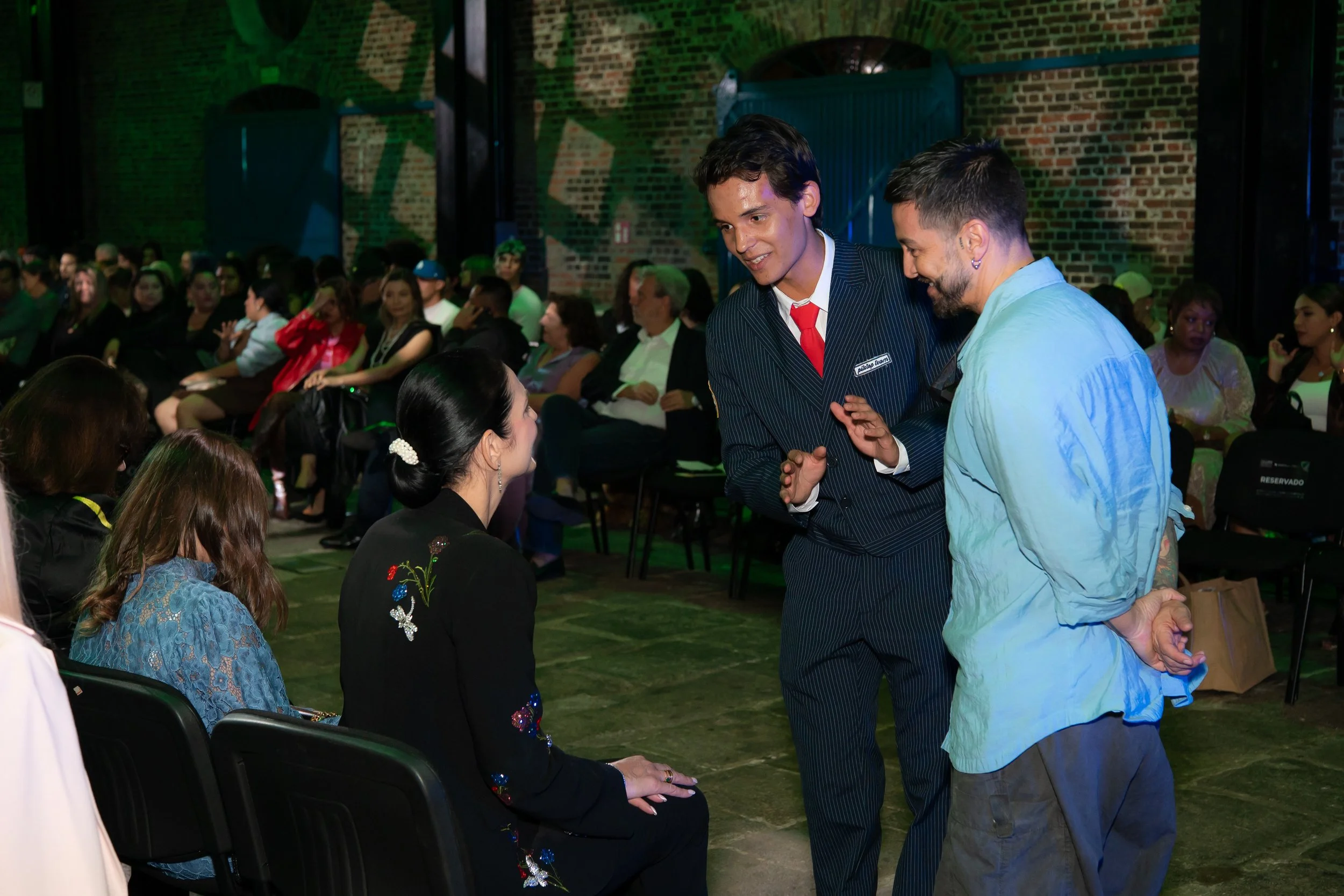 Personas conversando en una reunión en un espacio con paredes de ladrillo y sombra de luces proyectadas.