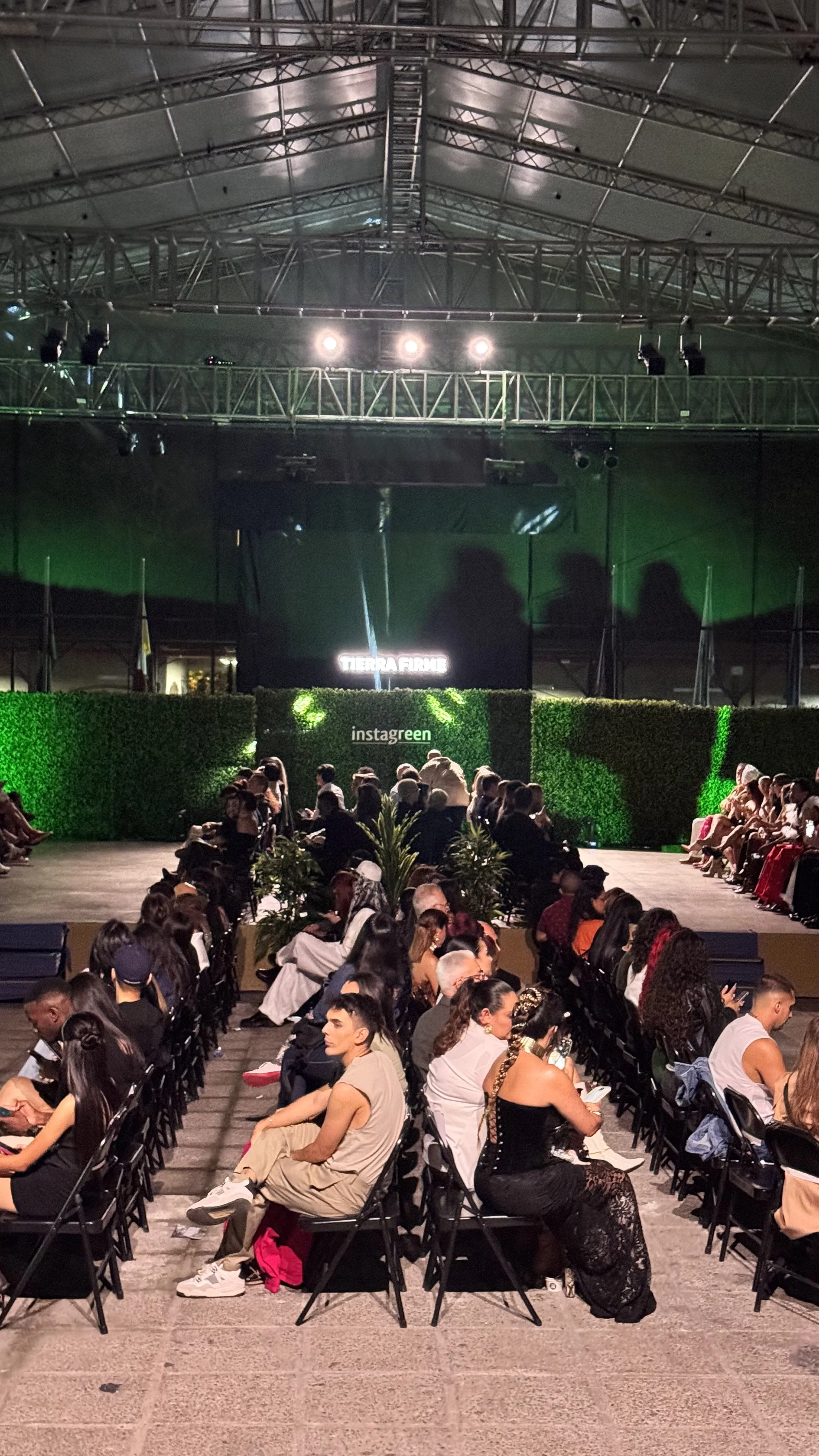 Imagen de un evento con muchas personas sentadas en sillas en un auditorio, con un escenario iluminado y pantallas digitales en el fondo.