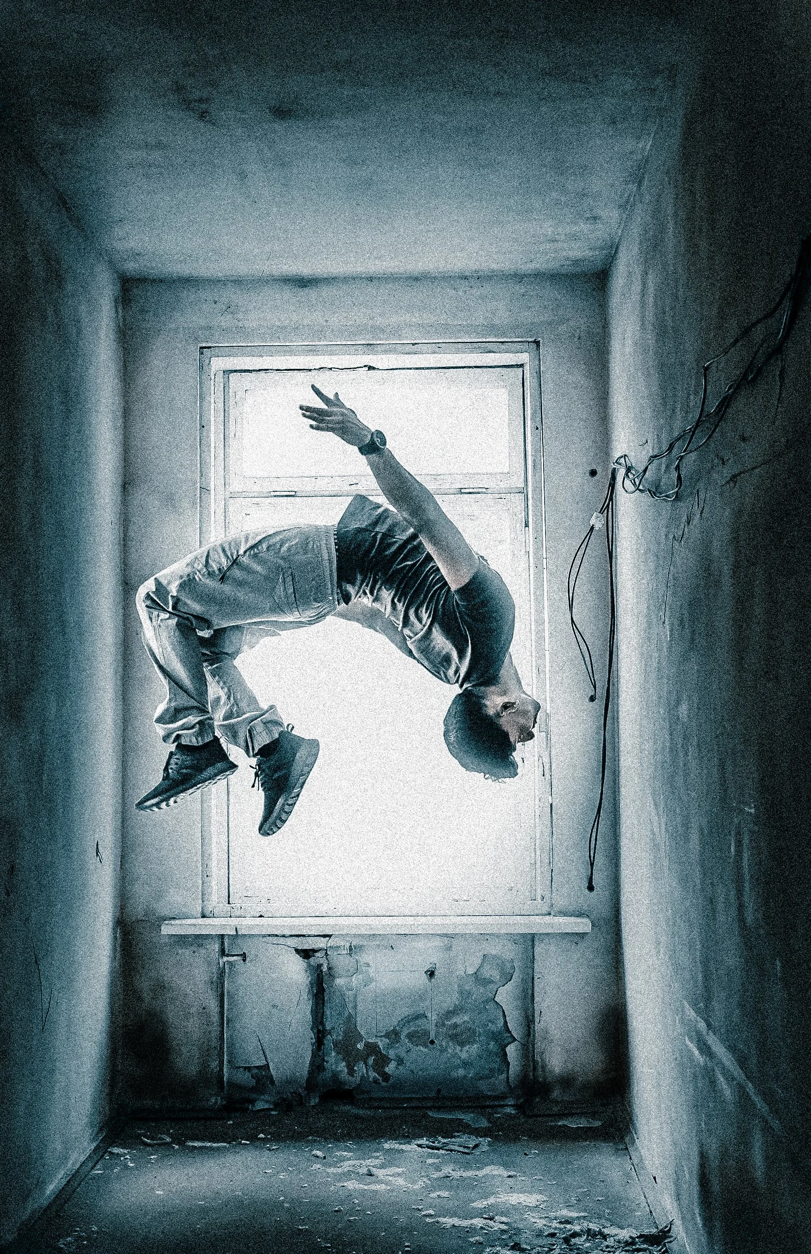 A person performing a backbend yoga pose in an abandoned, dilapidated room with peeling paint and debris on the floor, backlit by a bright window.