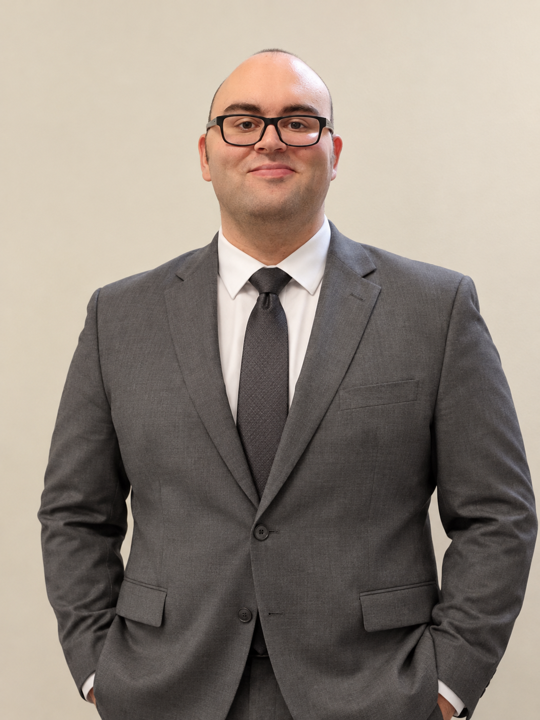 Professional man wearing glasses and a gray suit with a black tie, posing against a beige background