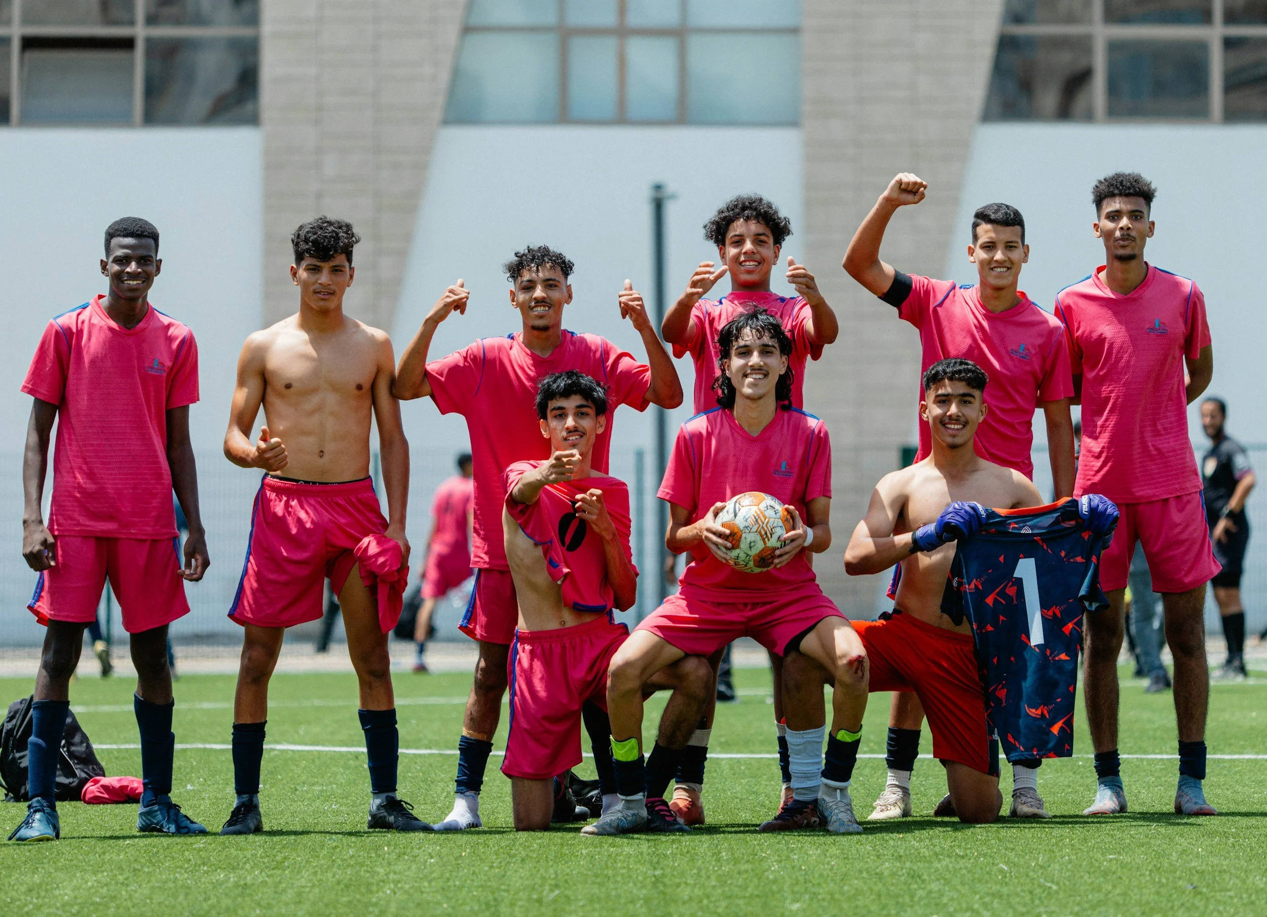 Youth soccer team in pink uniforms celebrating on a field, with players holding a soccer ball and goalkeeper jersey.
