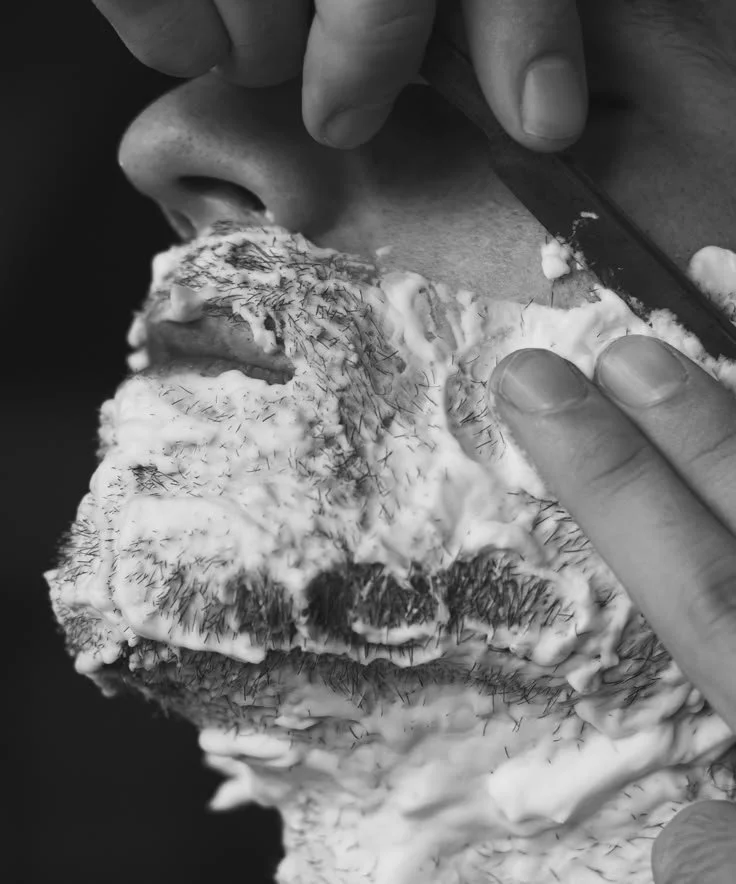 A person is carving or sculpting a large piece of white material, possibly foam or plaster, with a knife, focusing on detailed work around the nose and mouth area.