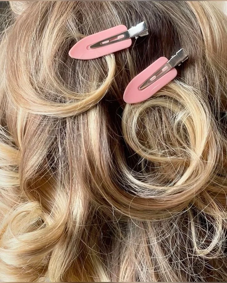 Close-up of blonde curly hair with two pink hair clips clipped onto the strands.
